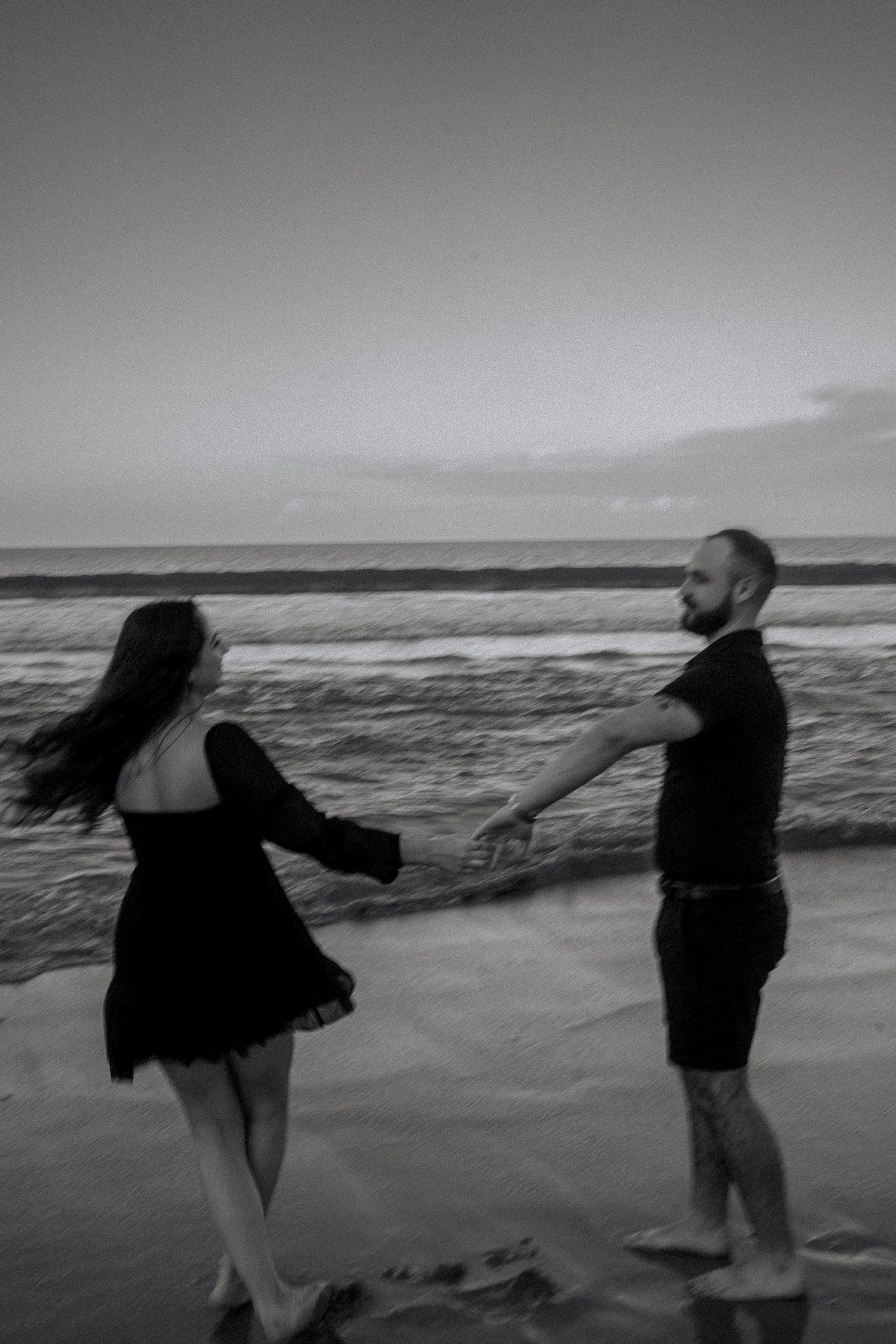 Black and white photo of a couple dancing on a beach at sunset, waves crashing in the background.