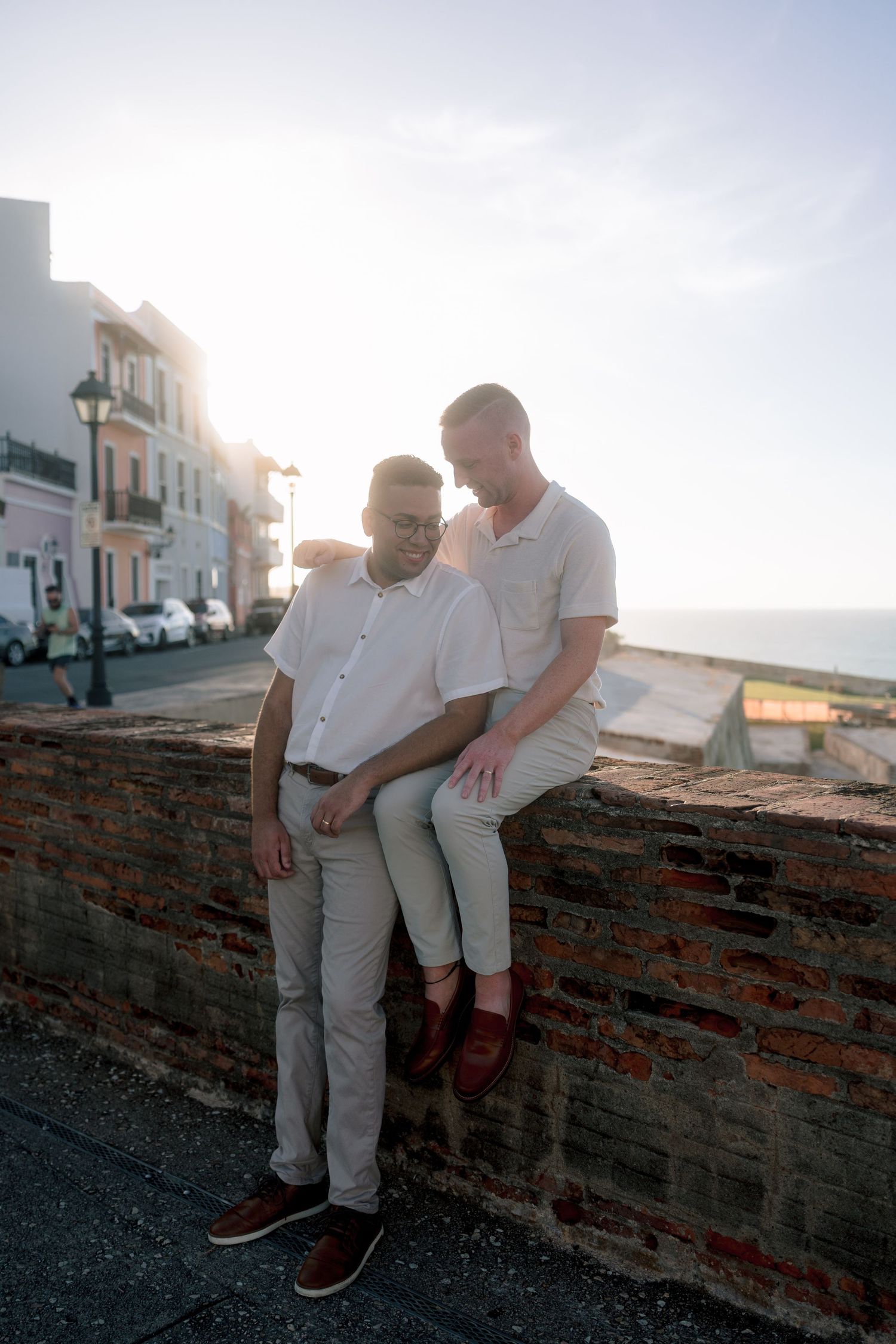 Couple poses romantically on ancient brick walls of Old San Juan with colorful colonial buildings at sunset.