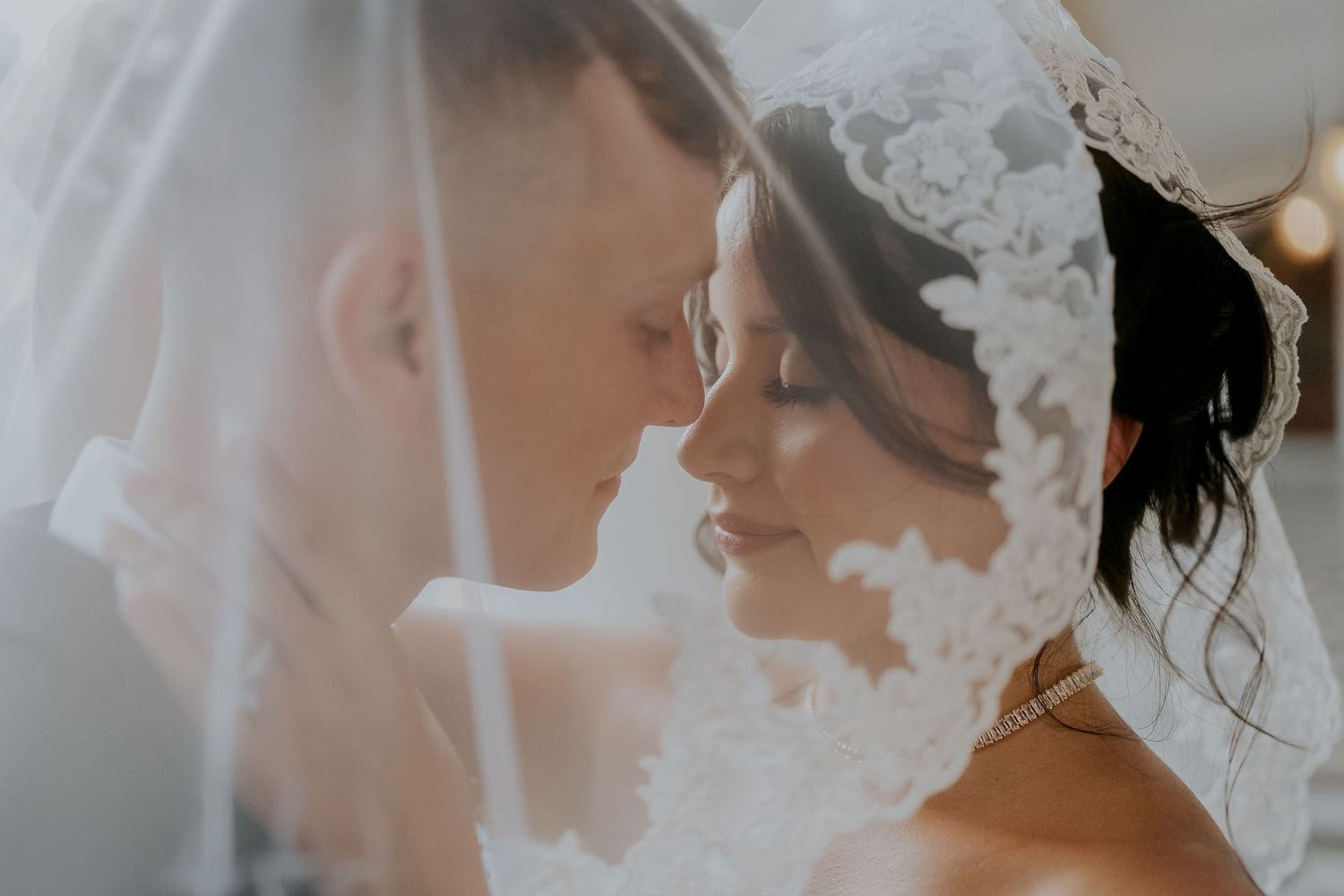 Bride and groom share an intimate moment under a lace wedding veil.