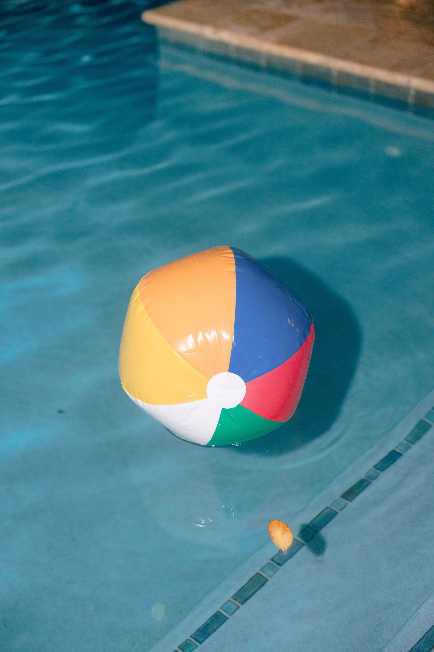 Colorful inflatable beach ball floating in a clear blue swimming pool on a sunny day.