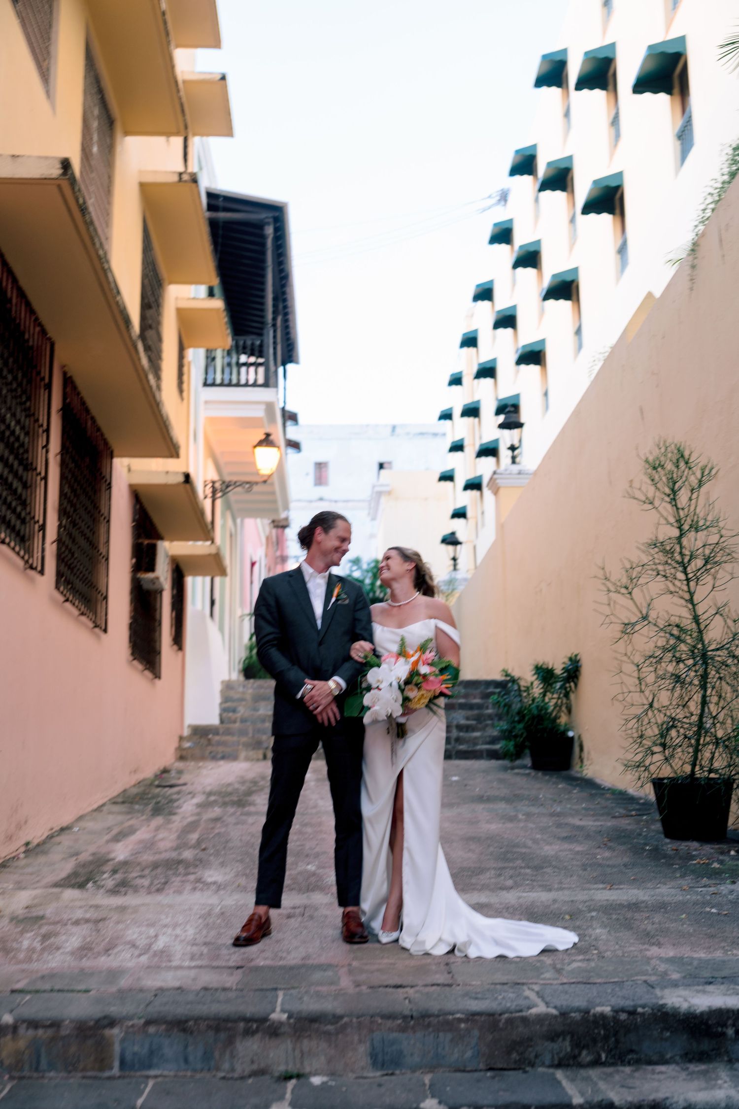 Bride and groom smiling at each other on a charming alleyway with colorful buildings in Old San Juan.