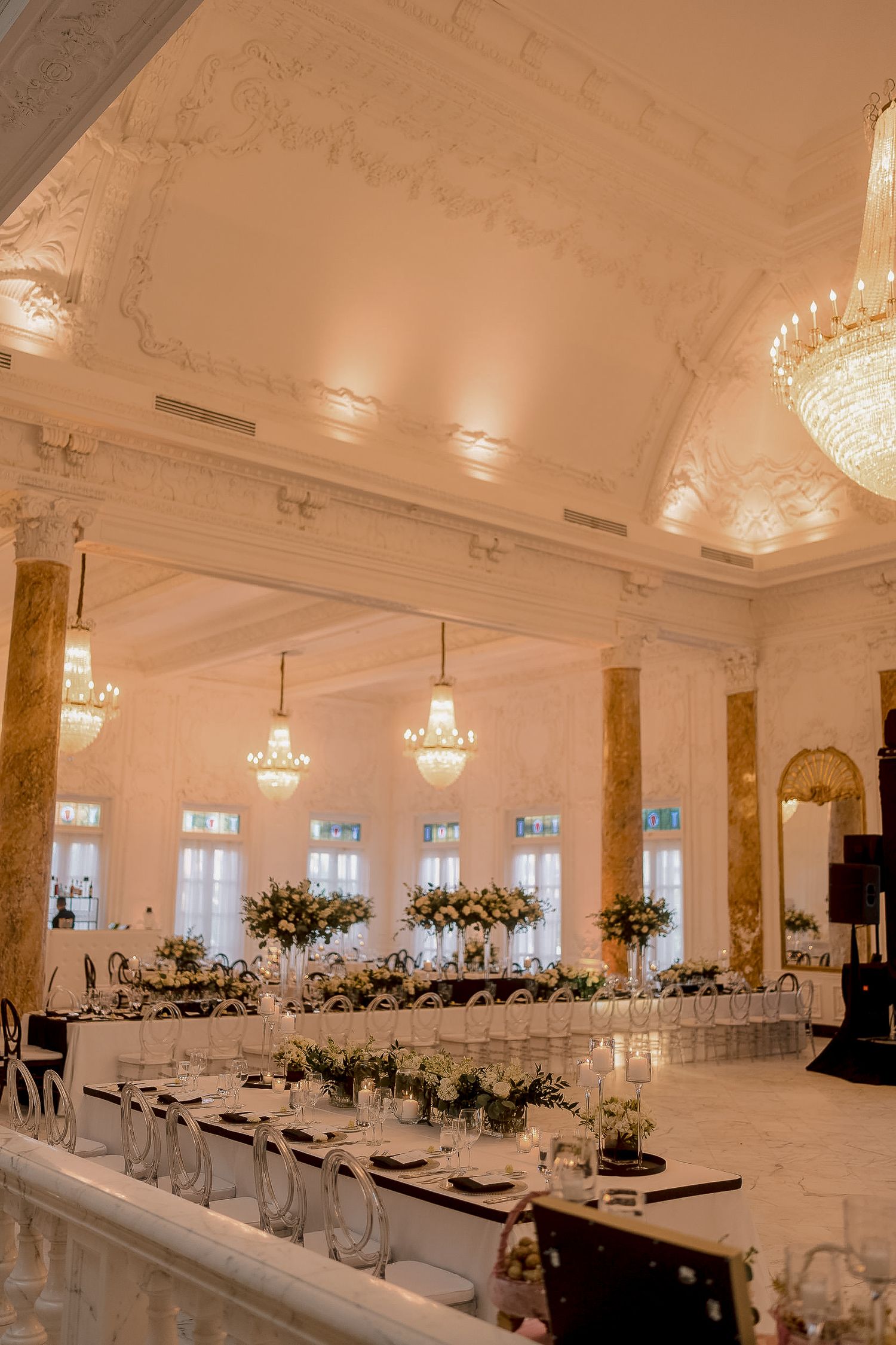 Grand ballroom wedding reception with crystal chandeliers and long floral centerpieces.