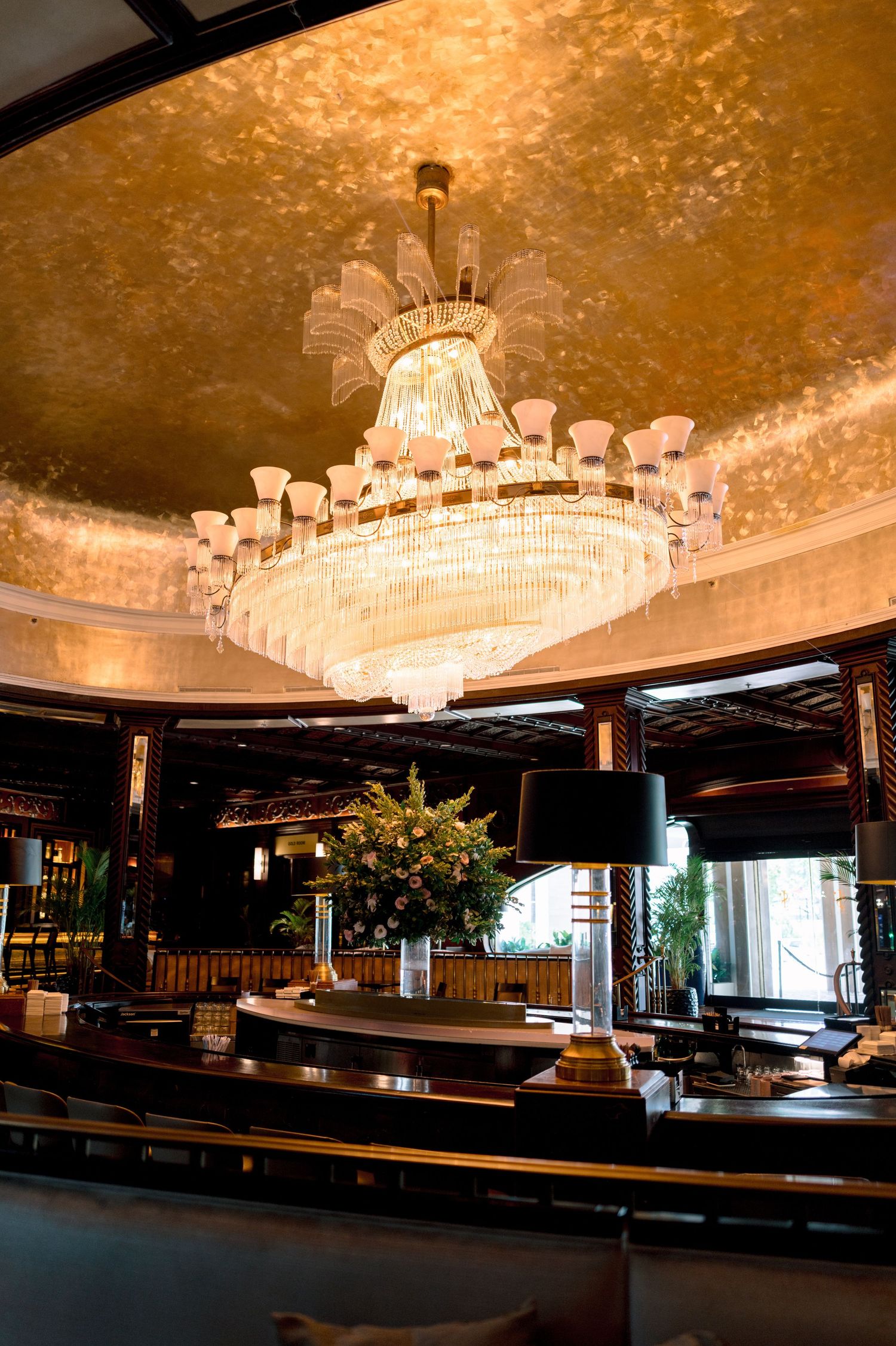 Elegant hotel lobby with a grand crystal chandelier hanging from a gold leaf ceiling above a curved reception desk.