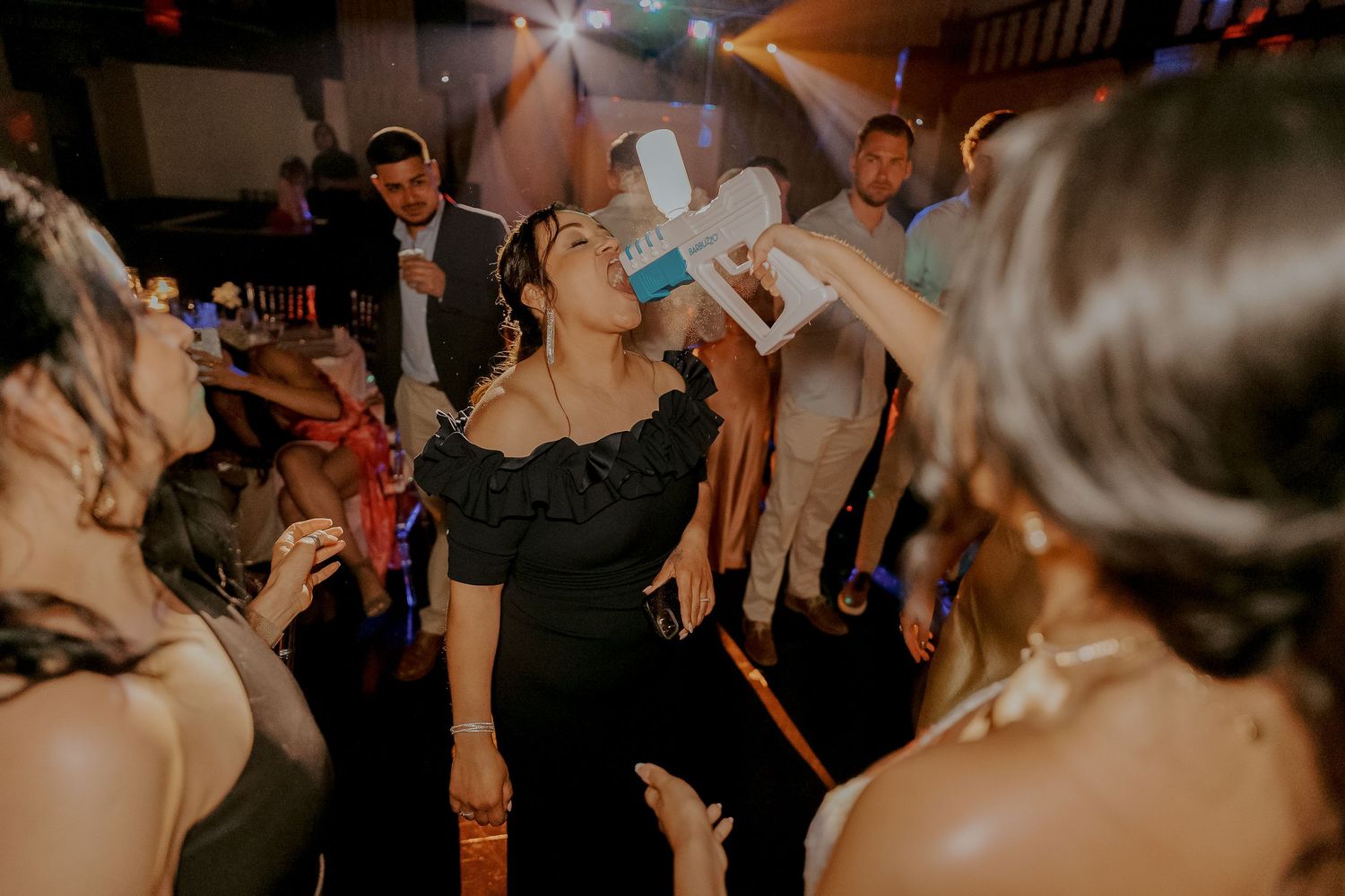 Wedding guest drinking from large novelty cup on dance floor at energetic nighttime reception.