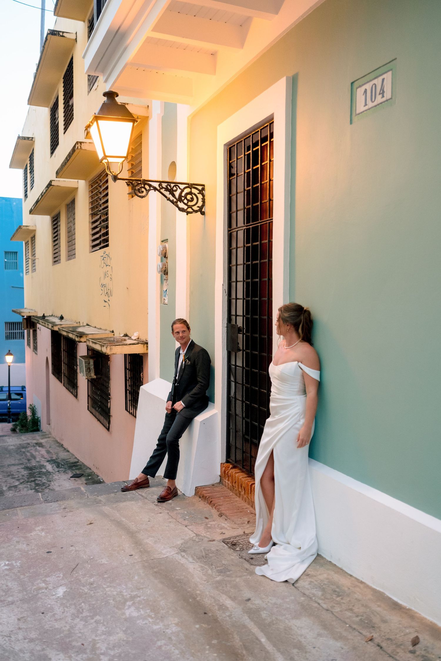 Bride and groom pose on colorful Old San Juan street at dusk beside glowing lantern.