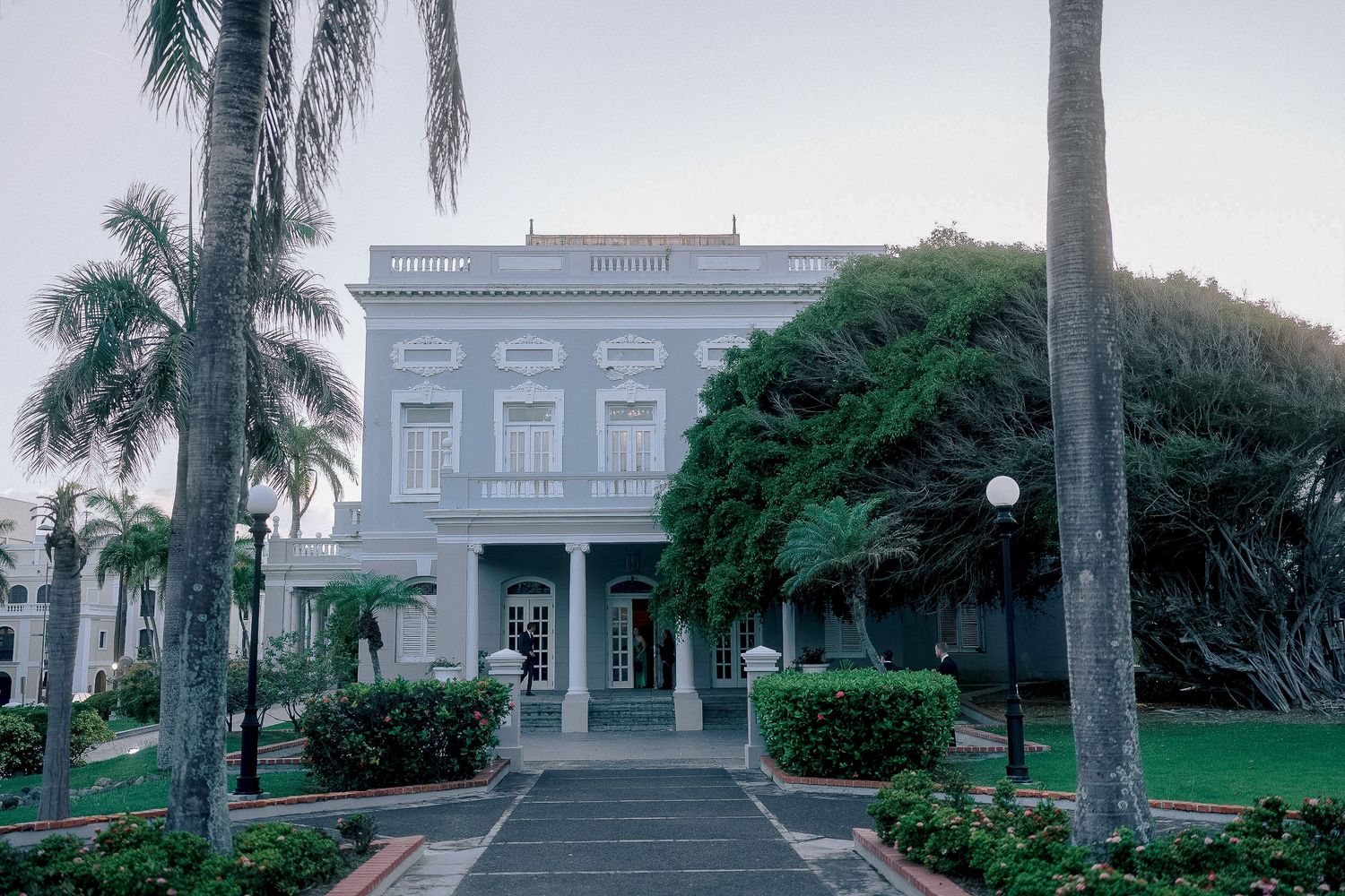 Grand white colonial building with palm trees and manicured gardens at dusk wedding venue exterior.