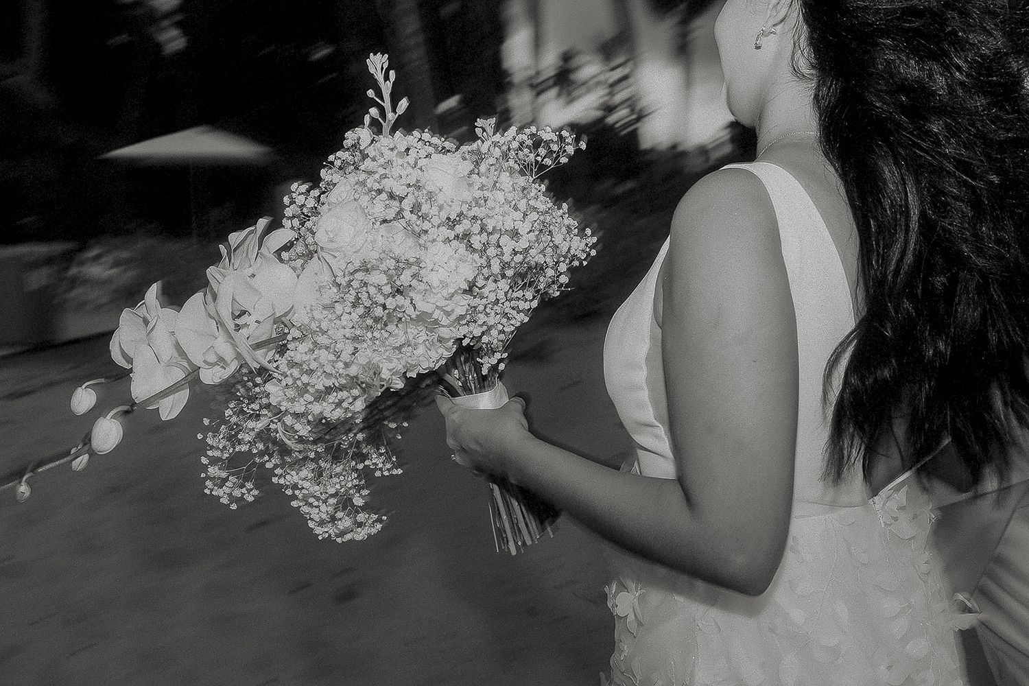 Black and white photo of a bride in a white dress holding a large floral bouquet with baby's breath.