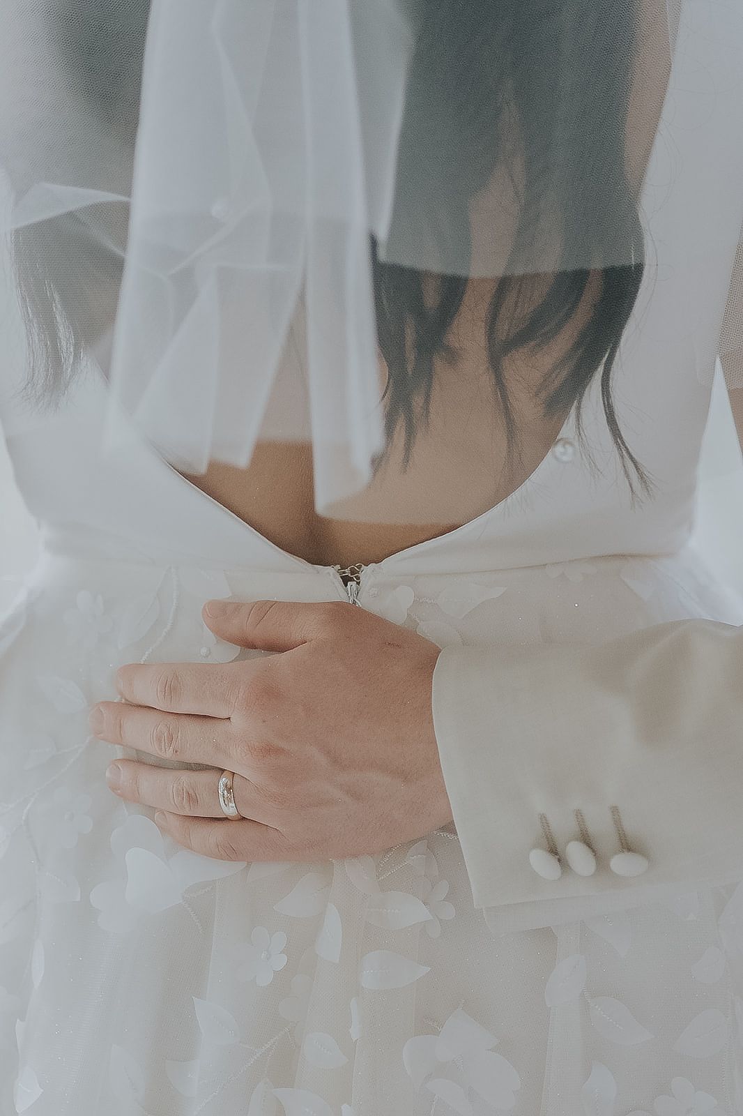 Close-up of groom holding bride at waist showing wedding rings and veil.