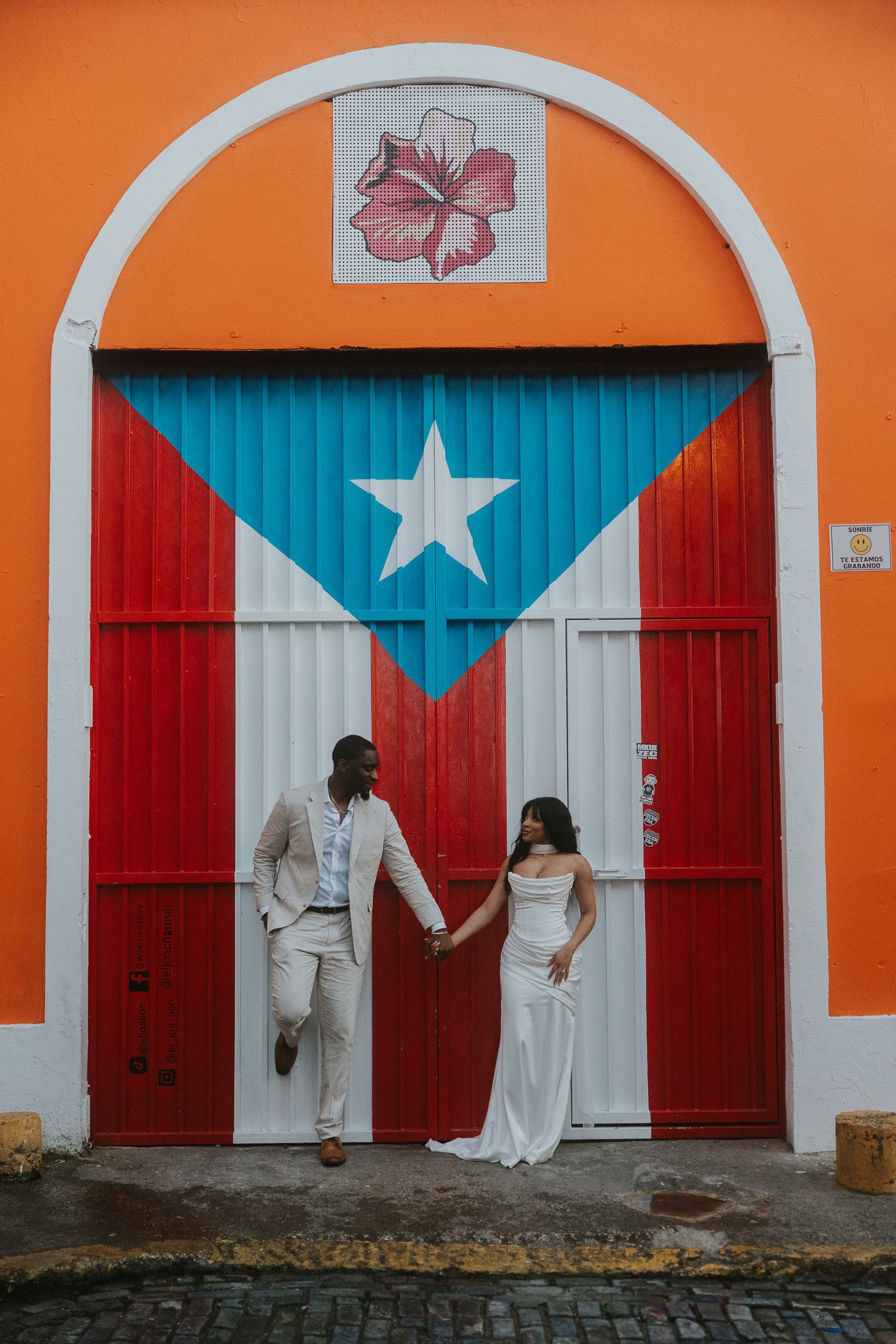Couple holding hands in front of a Puerto Rico flag painted door on a colorful orange wall in Old San Juan.