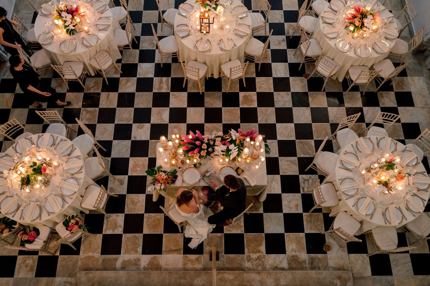 Aerial view of elegant wedding reception with checkered floor, candlelit round tables, and floral centerpieces.