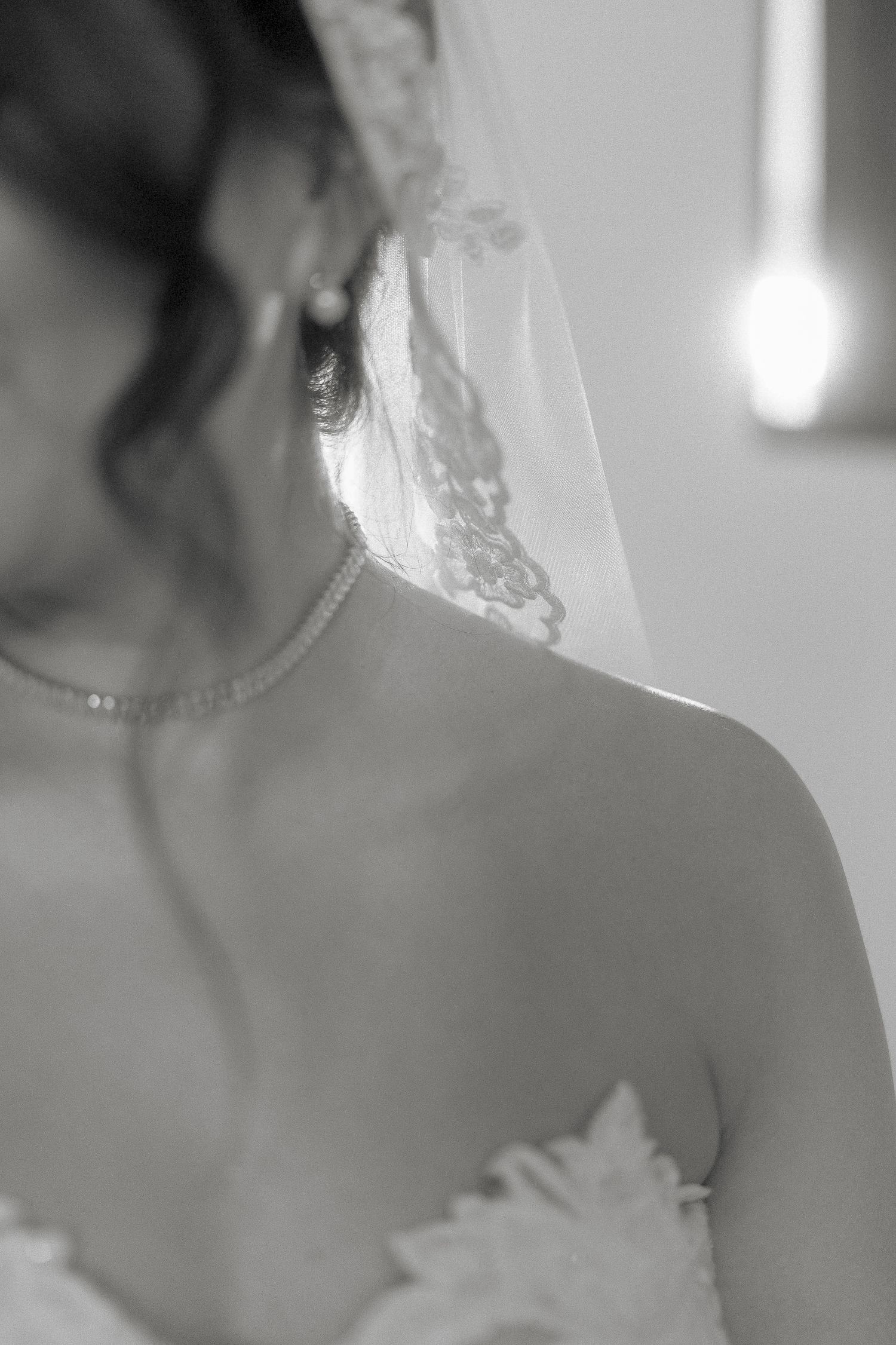 Black and white close-up of a bride wearing a lace veil, pearl earring, and delicate necklace.