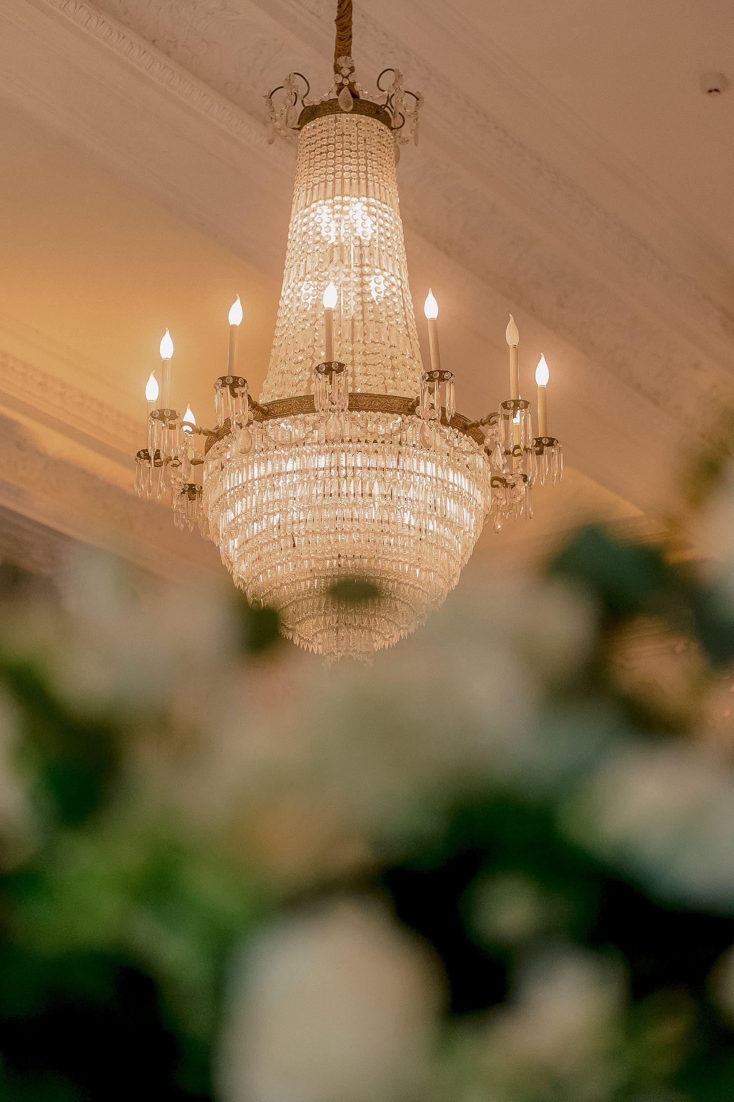 Ornate crystal chandelier with candle lights hanging above white floral arrangements at a wedding reception.