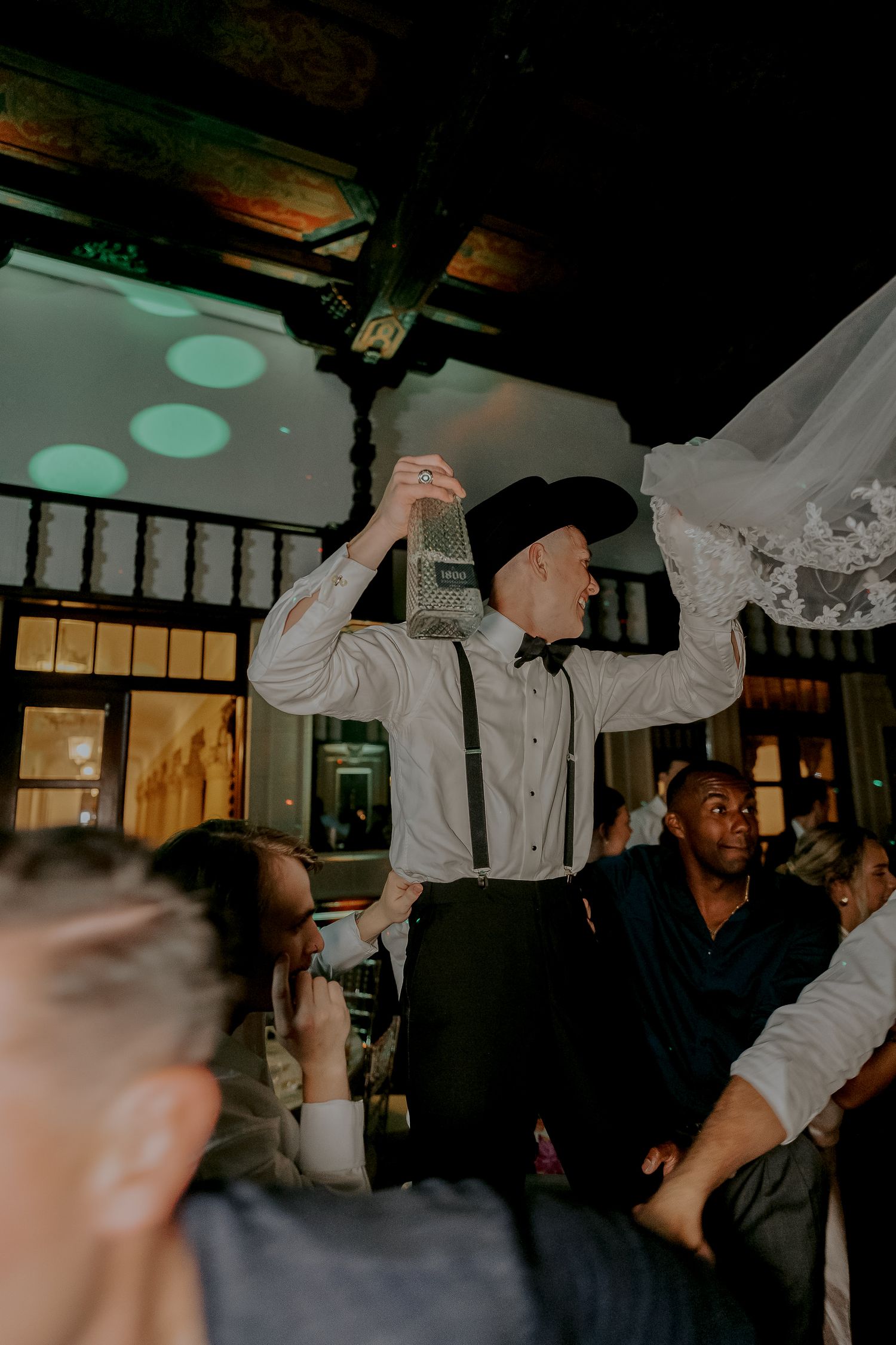 Guest dances energetically holding bride's veil at lively wedding reception.