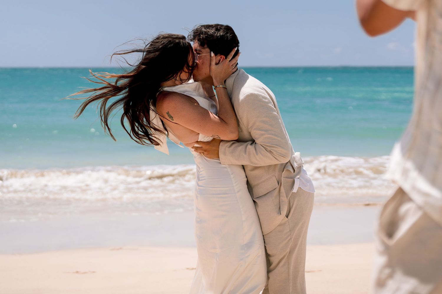 Couple sharing a romantic kiss on a tropical beach during their destination wedding ceremony.