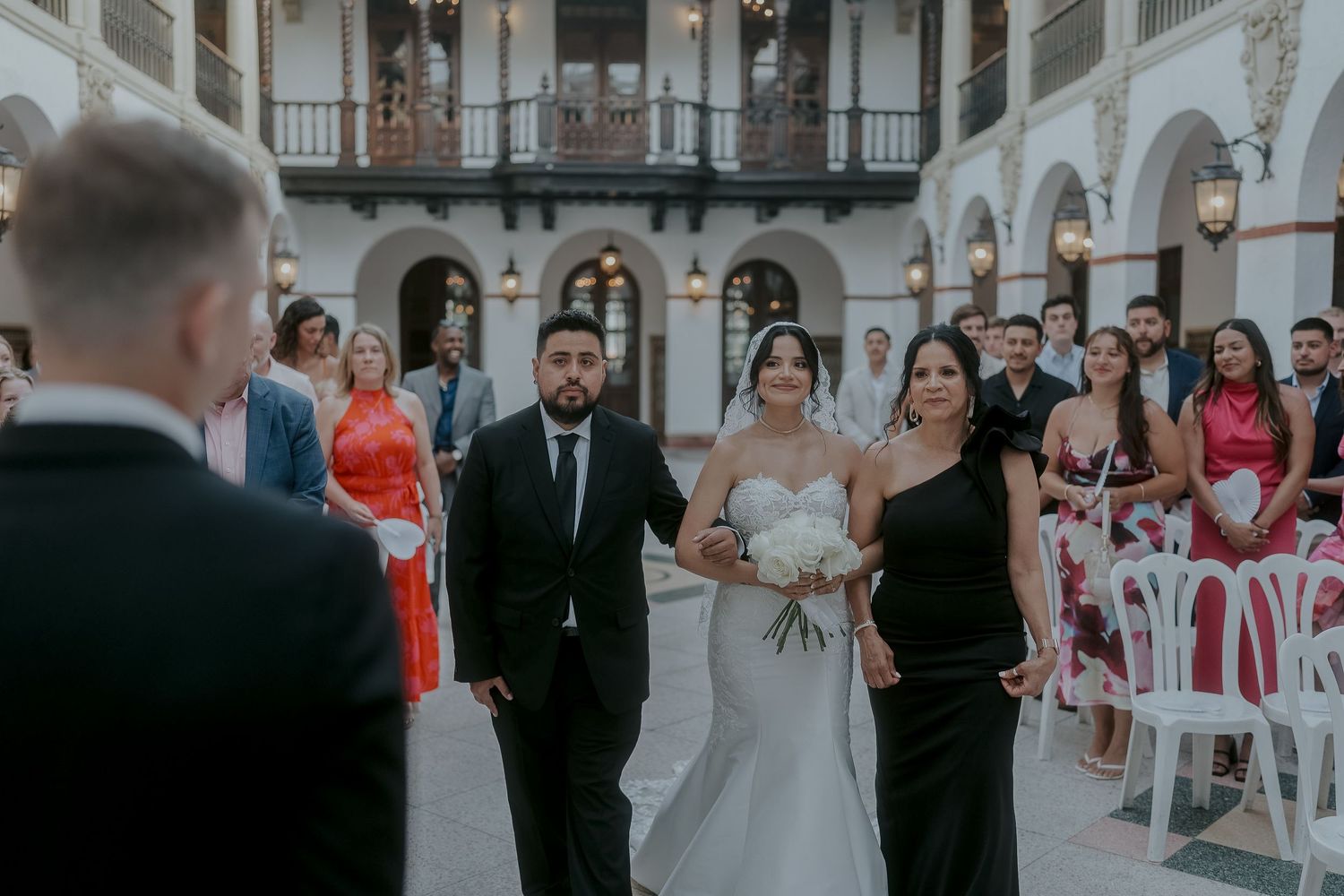 Bride walks down the aisle escorted by two family members at an elegant outdoor wedding ceremony.