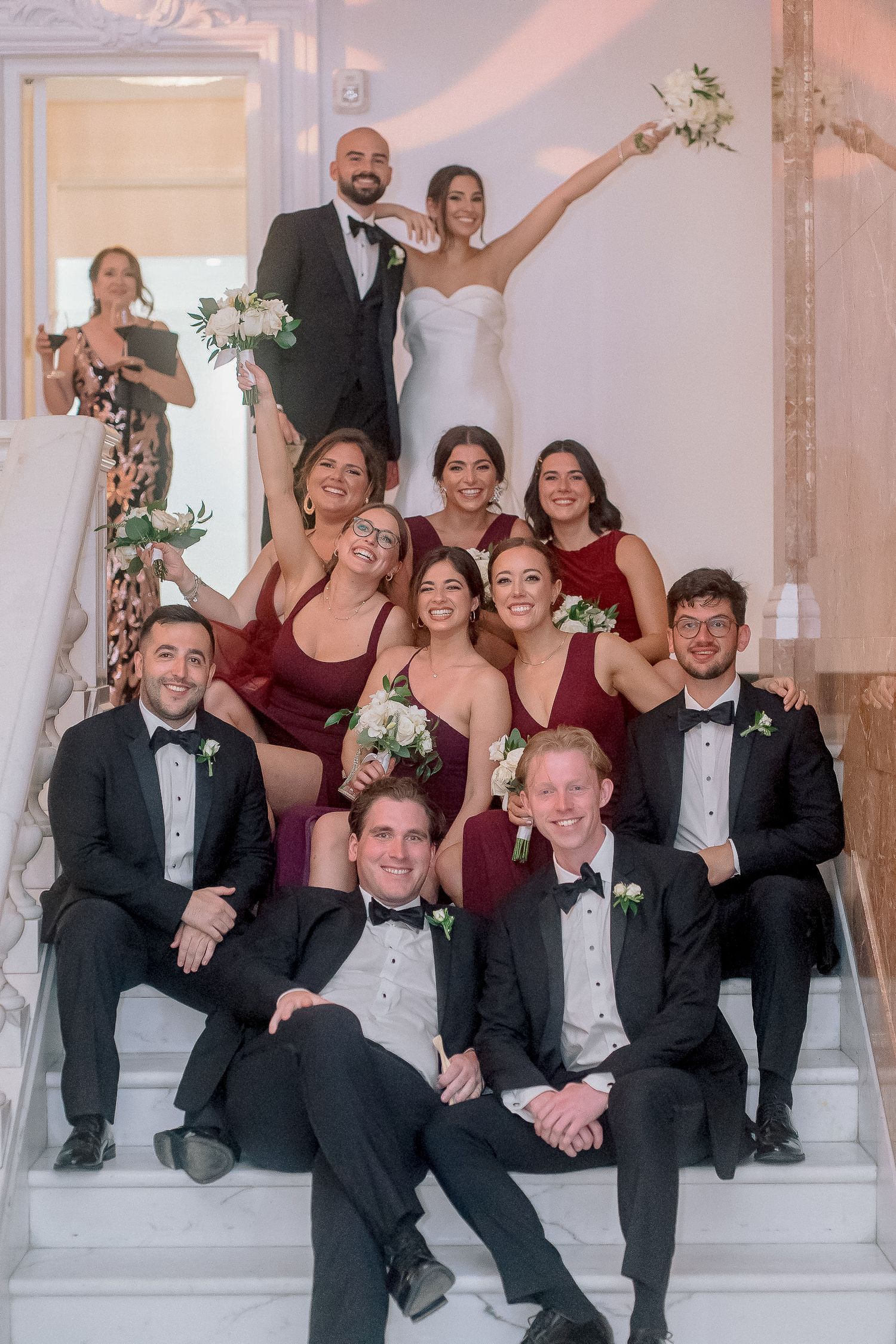 Wedding party posing on grand staircase with bridesmaids in burgundy dresses and groomsmen in black tuxedos.