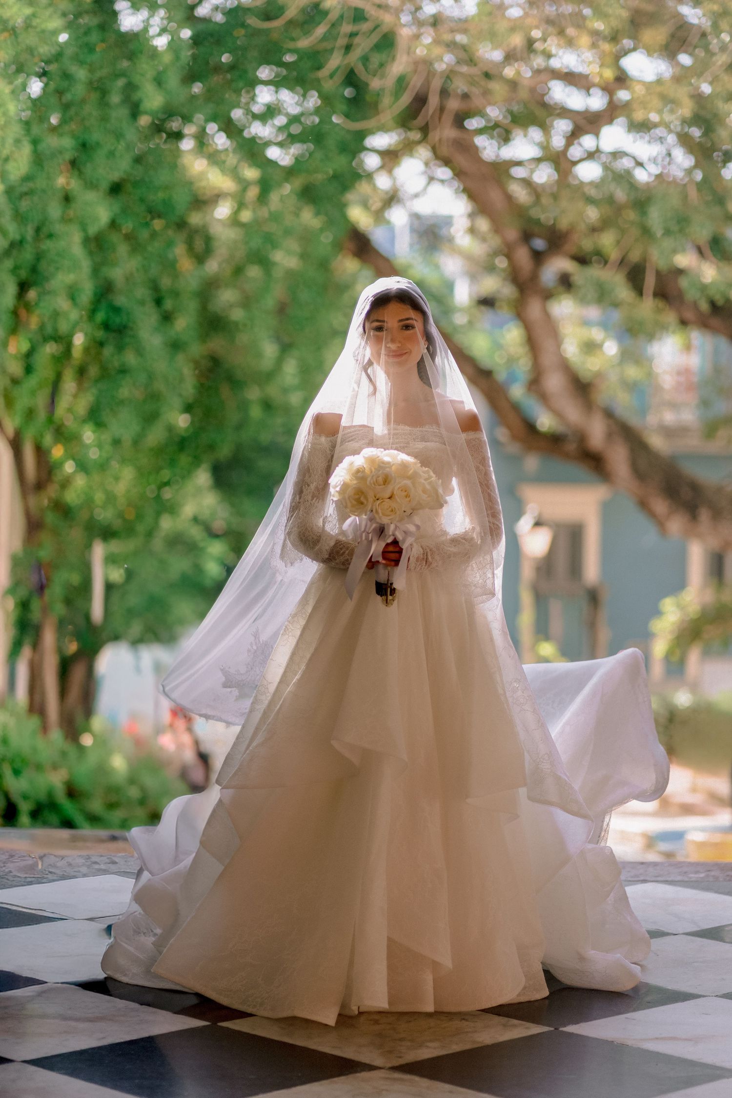 Bride in a white ball gown with veil holding bouquet outdoors.