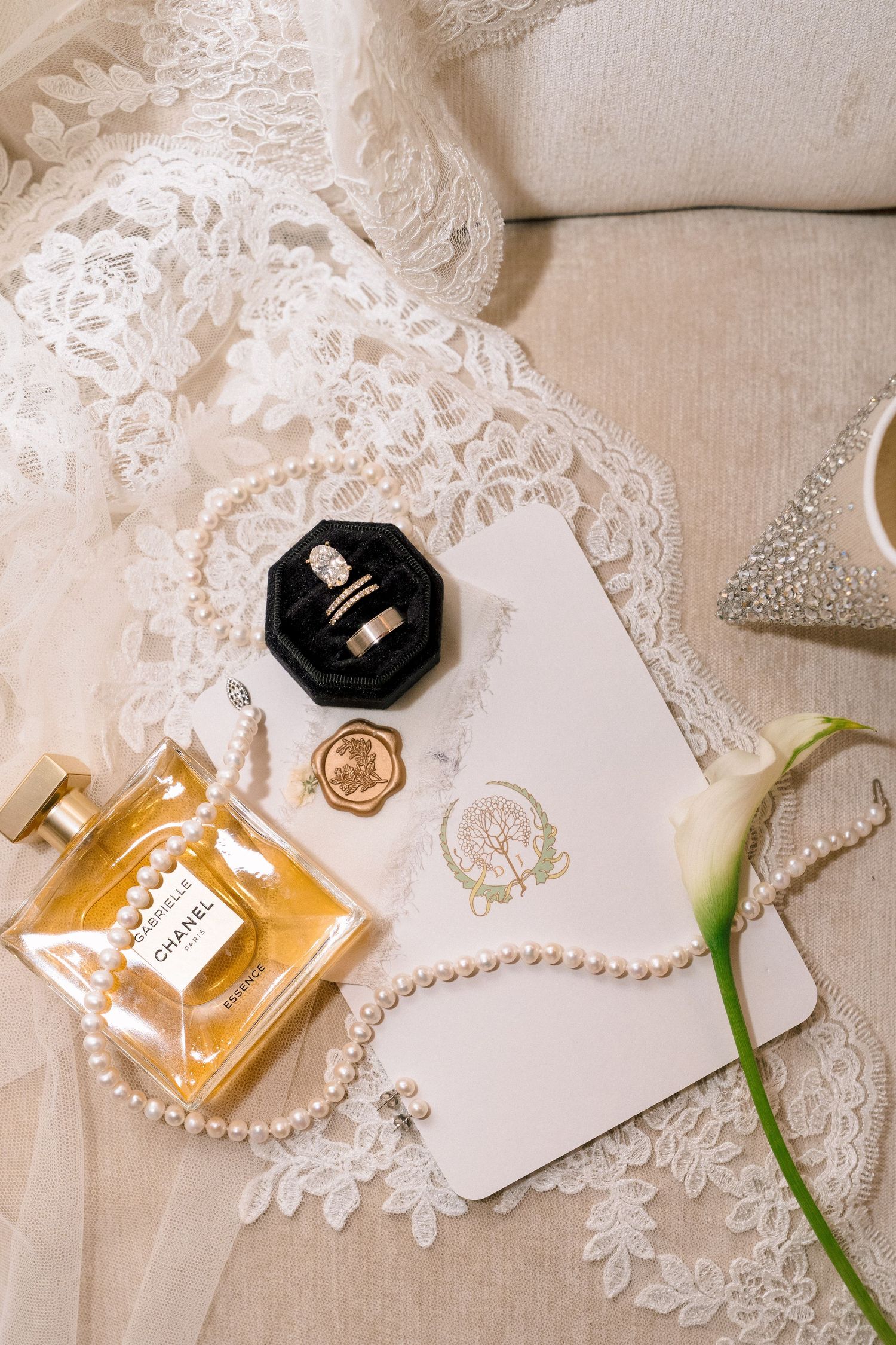 Luxury bridal flat lay with Chanel perfume, pearl necklace, wedding rings, and floral stationery.