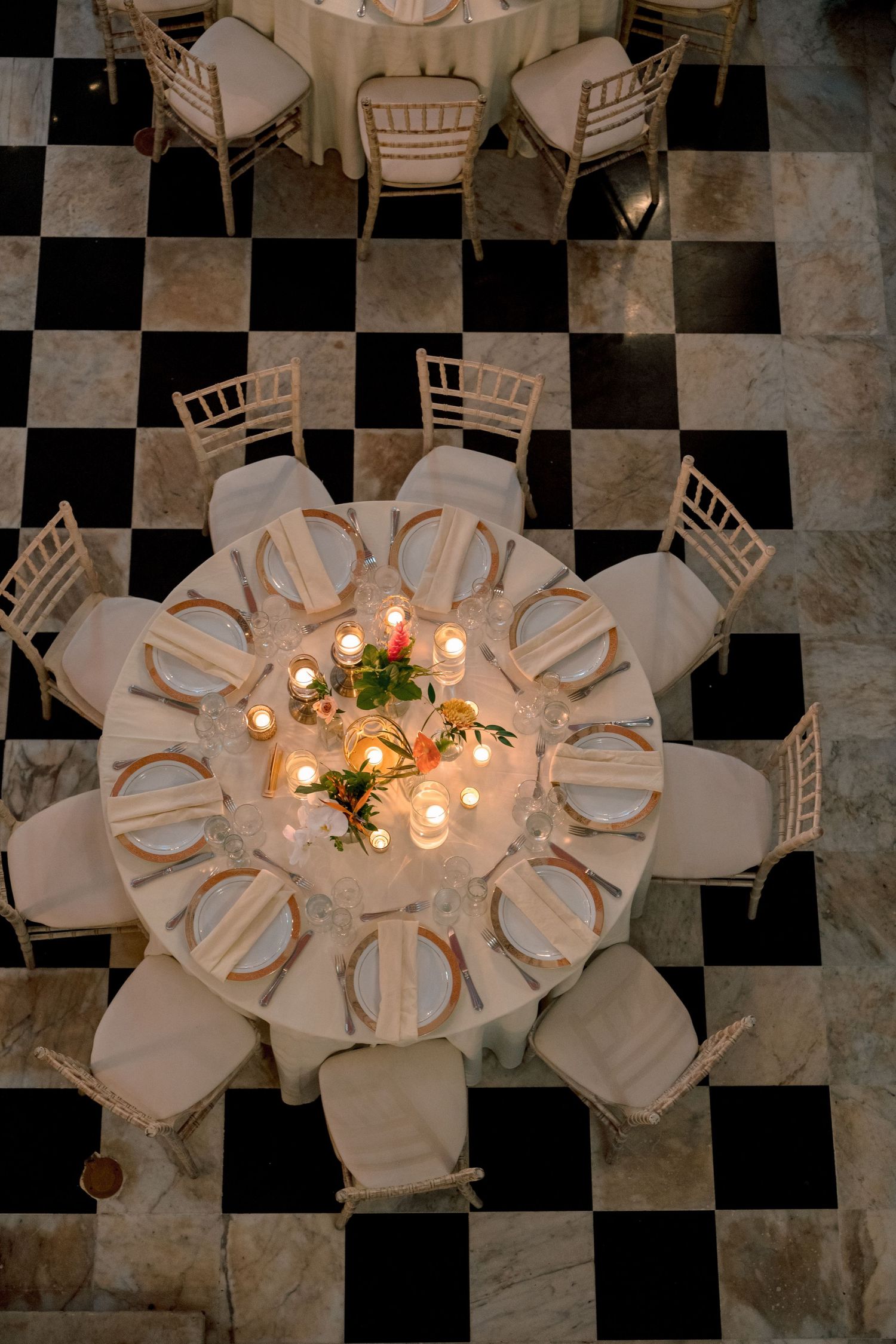 Aerial view of round wedding reception table with candle centerpiece on black and white checkered floor.