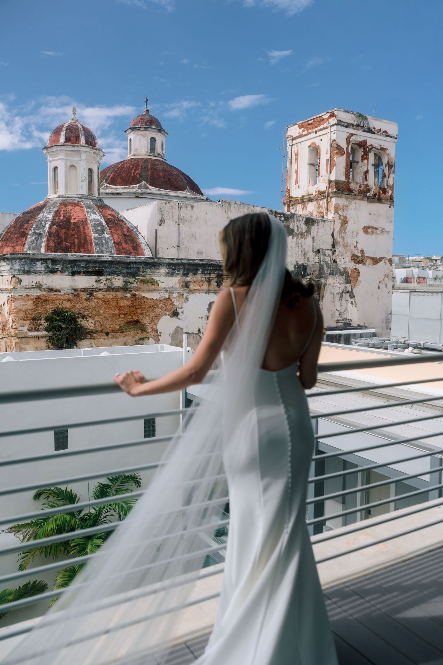 Bride in backless gown with veil on rooftop overlooking historic church domes.