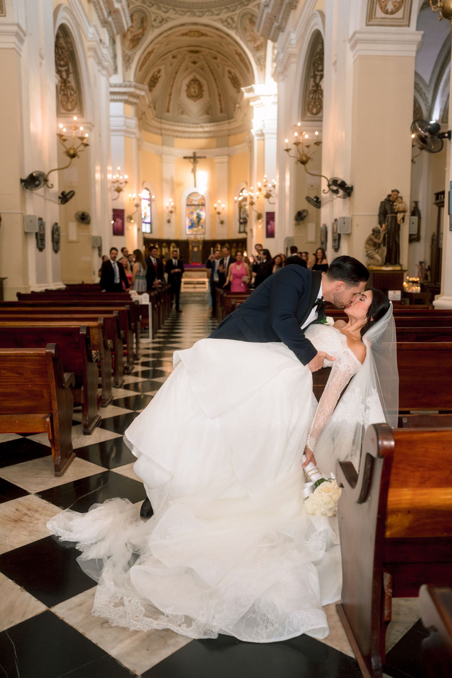 Bride and groom share a romantic dip kiss in a stunning church aisle after their wedding ceremony.