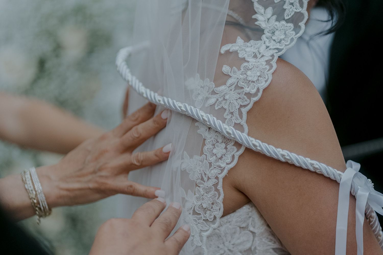 Hands adjusting a lace wedding dress with a rope tie detail on the back of a bride.