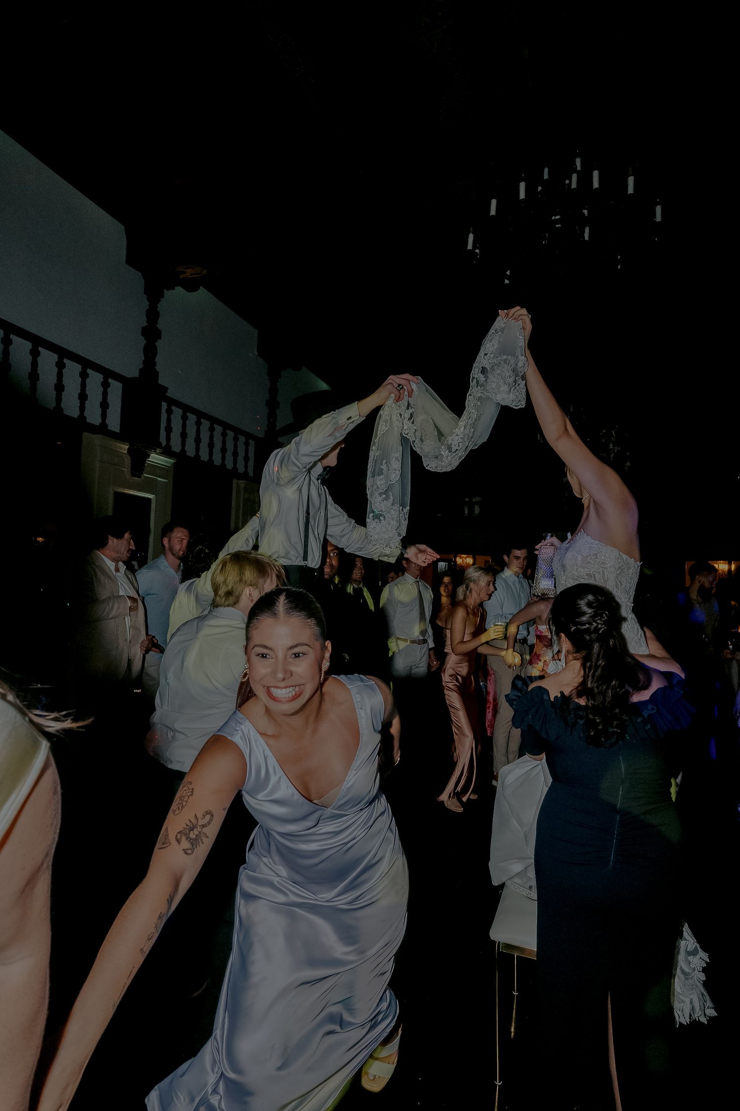 Smiling bridesmaid in silver gown dances at lively wedding reception.