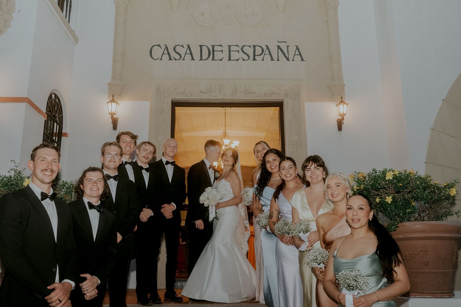 Wedding party poses together in front of Casa de Espana entrance with bridesmaids in sage green dresses.