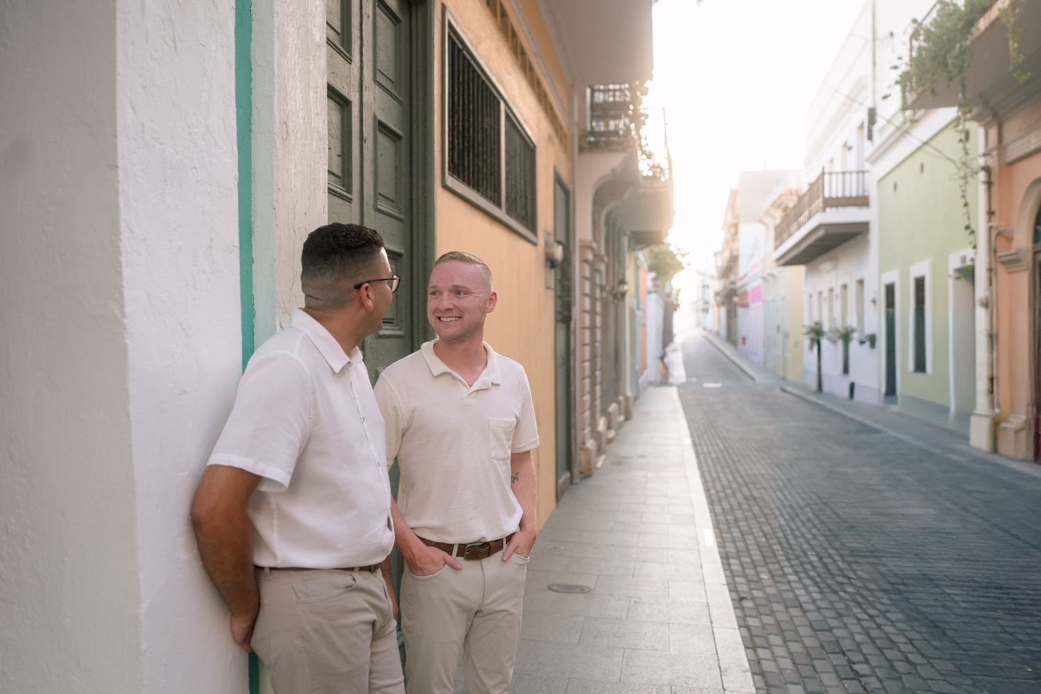 Two men in white polo shirts chat on a sunlit cobblestone street in Old San Juan, Puerto Rico.