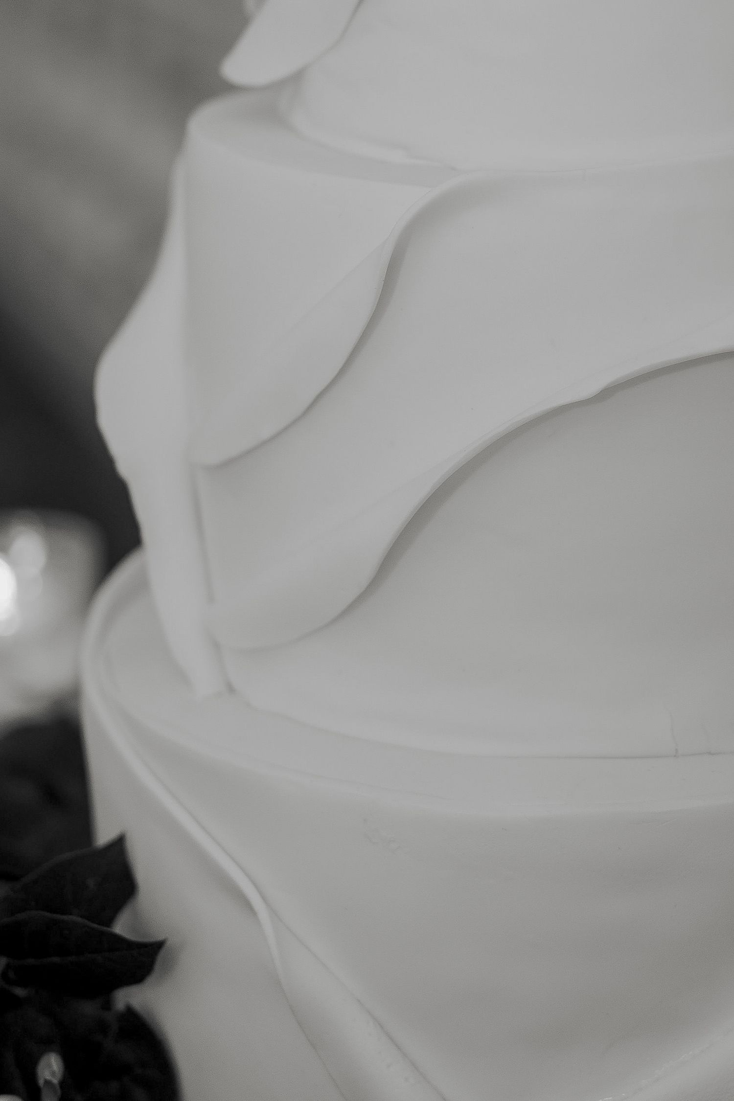 Close-up black and white photo of a tiered white fondant wedding cake with elegant ruffled details.