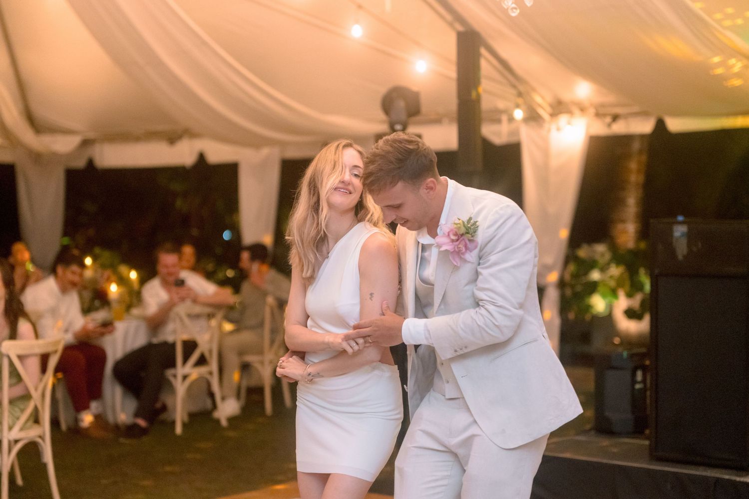 Bride in short white reception dress laughs joyfully with groom during lively wedding reception dance.