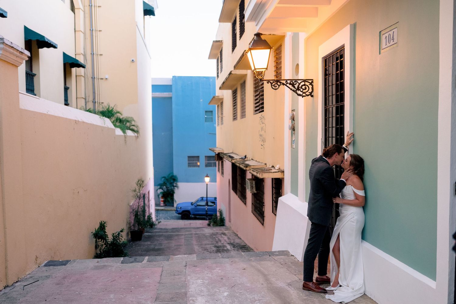 Wedding couple shares a kiss in a colorful narrow alley with pastel-colored buildings in Old San Juan, Puerto Rico.