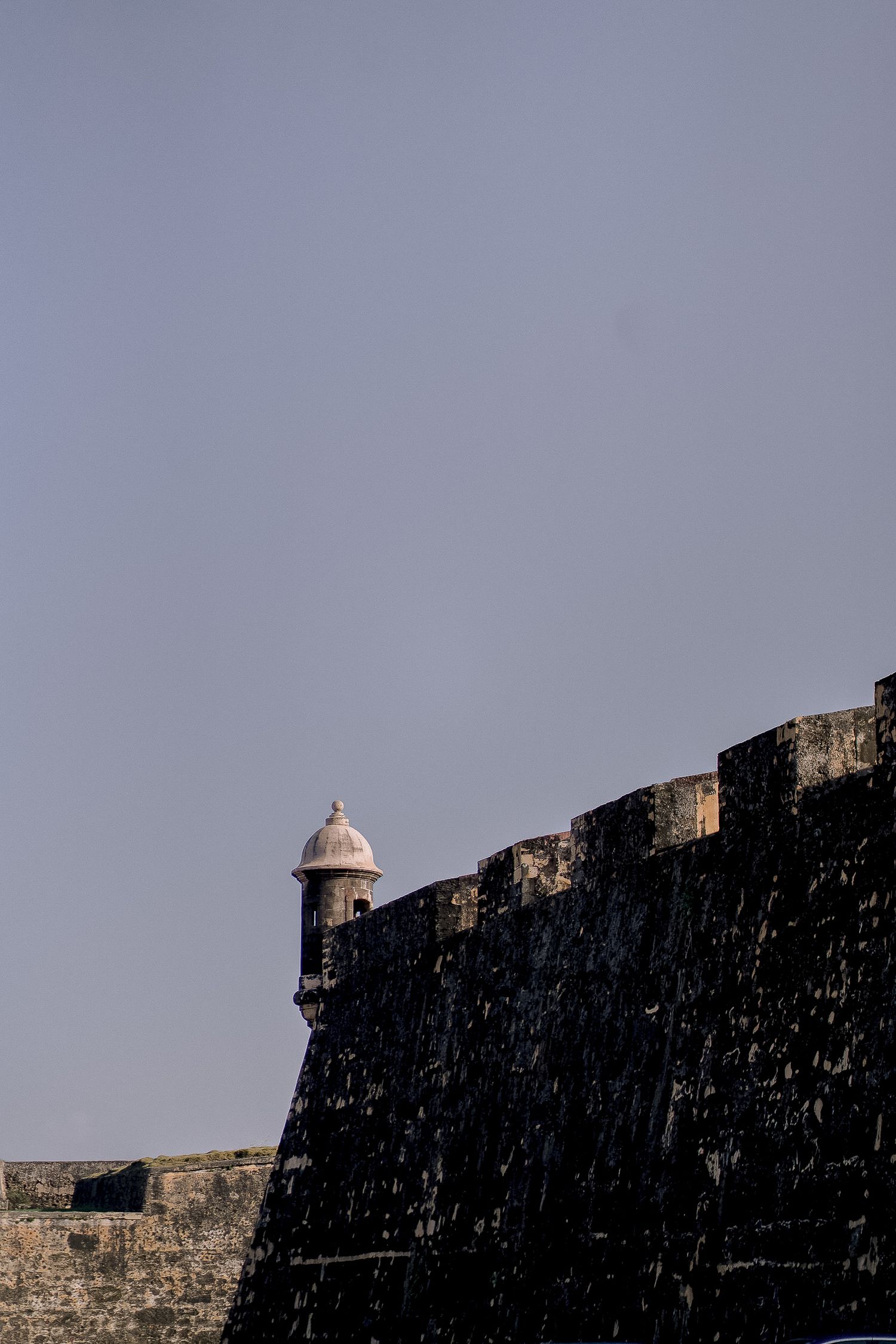 Historic stone fort wall with a sentry box turret against a clear blue sky.