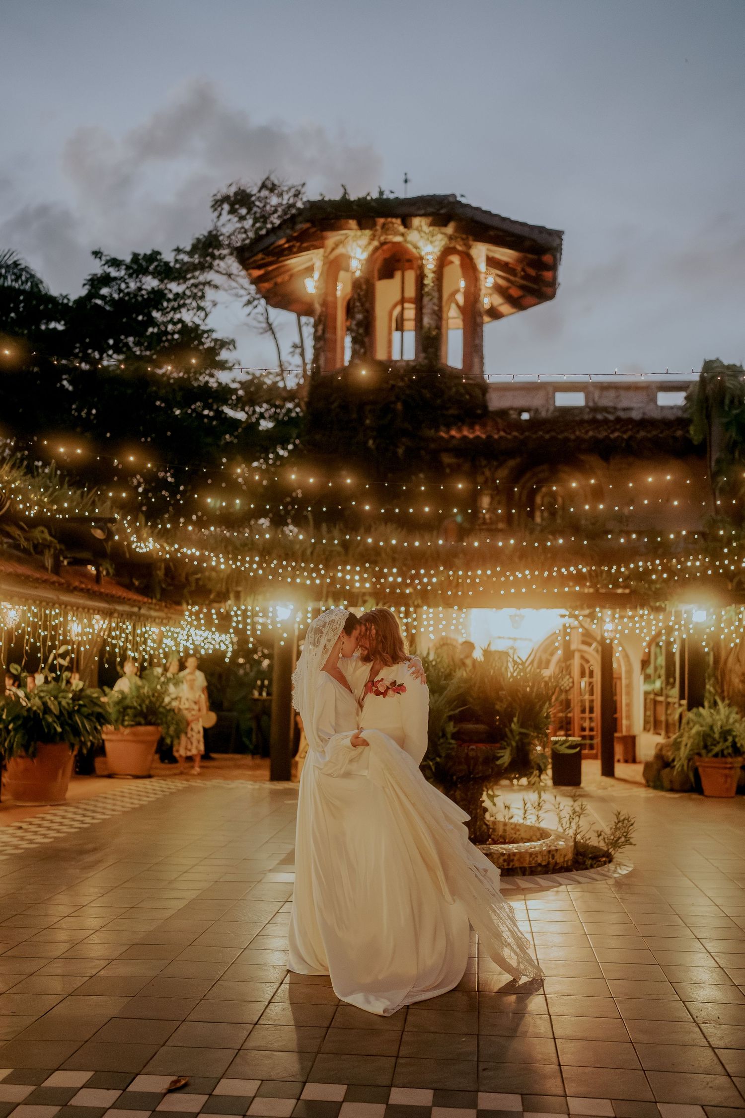Couple shares first dance under string lights at romantic outdoor wedding venue at dusk.