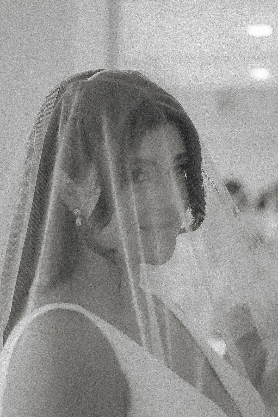 Elegant bride wearing veil over face in soft black and white portrait.