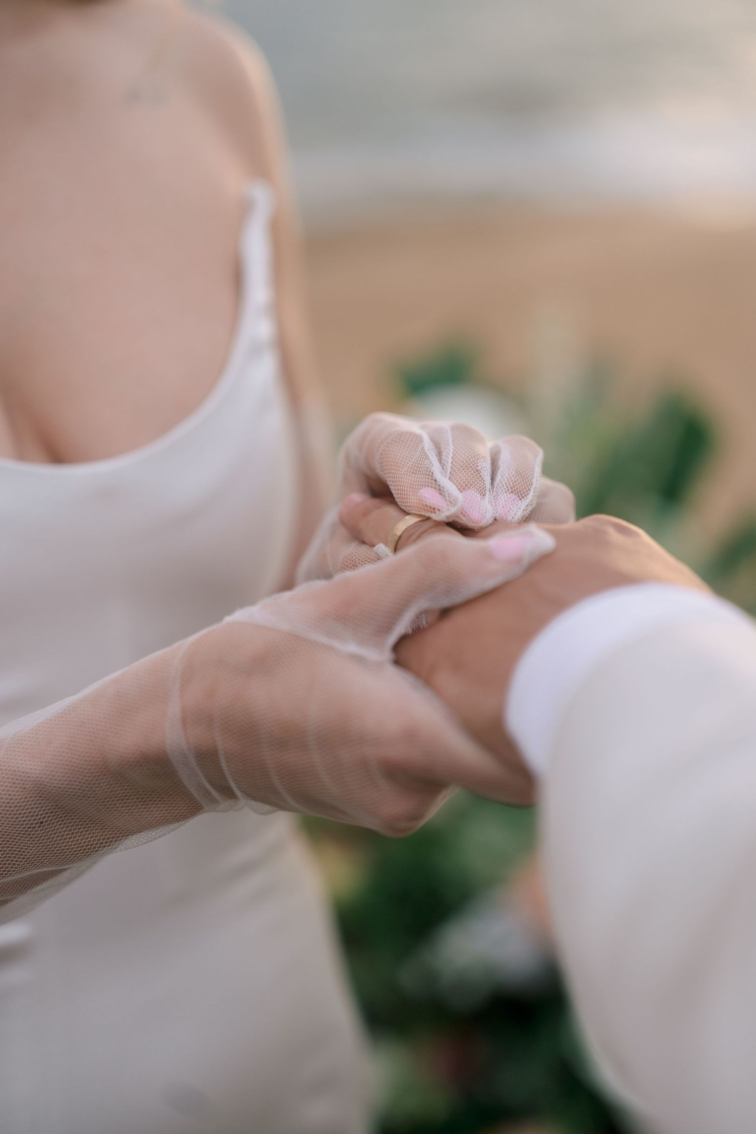 Close-up of bride in sheer gloves placing gold wedding ring on grooms hand during ceremony.