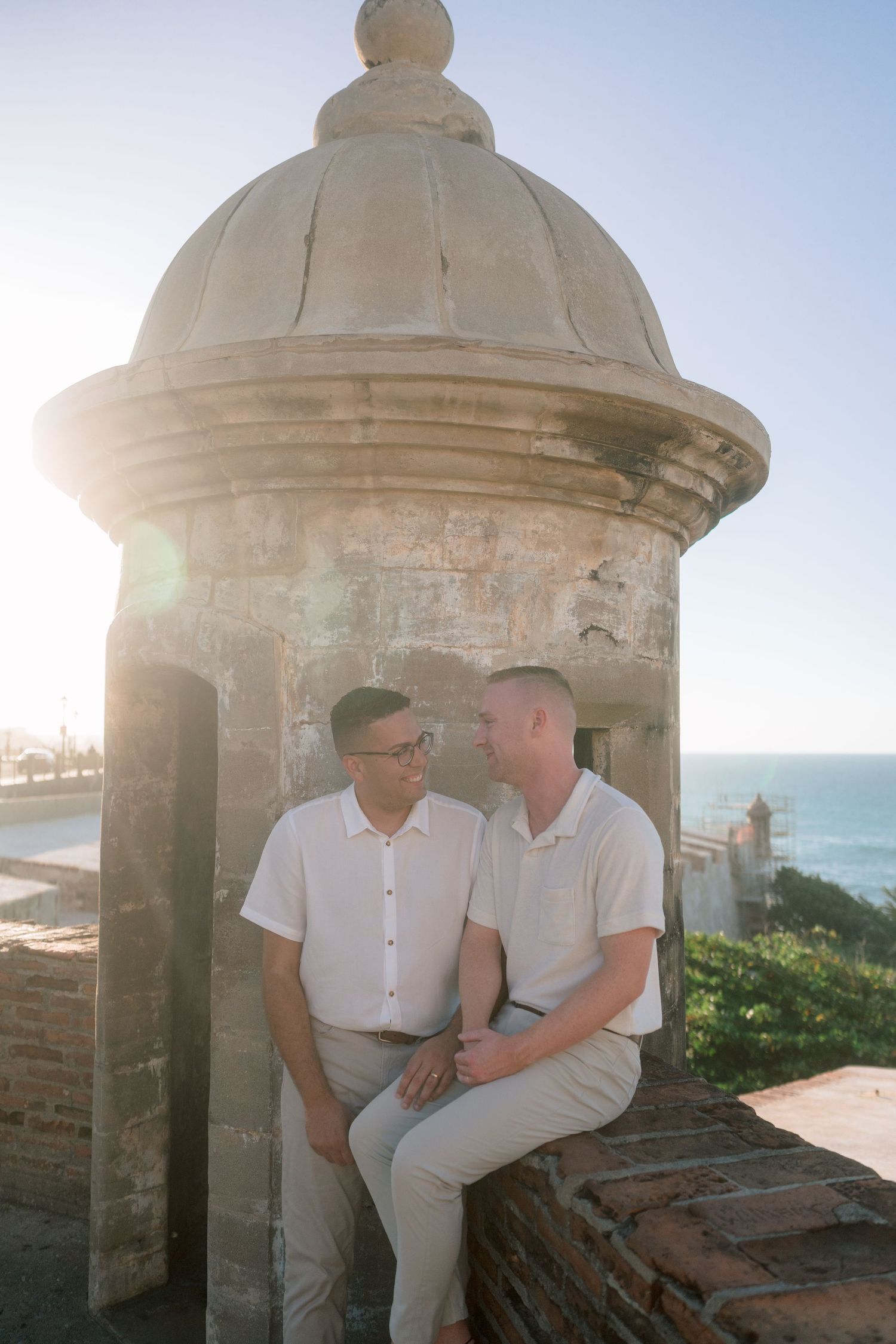 Two men share an intimate moment by a historic stone sentry box in Old San Juan, Puerto Rico at golden hour.