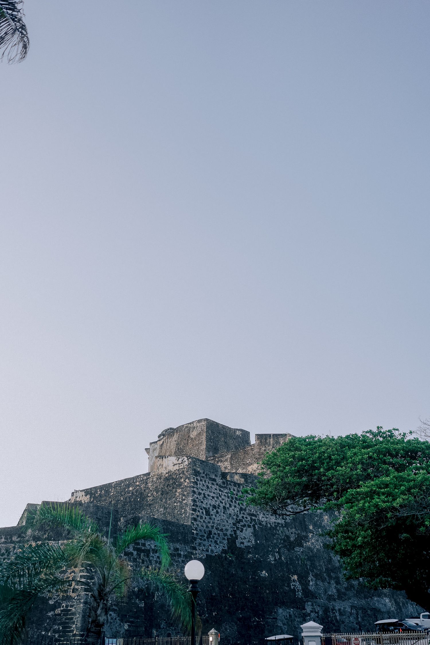 Ancient stone fortress with lush green trees against a clear sky, historic colonial architecture landmark.