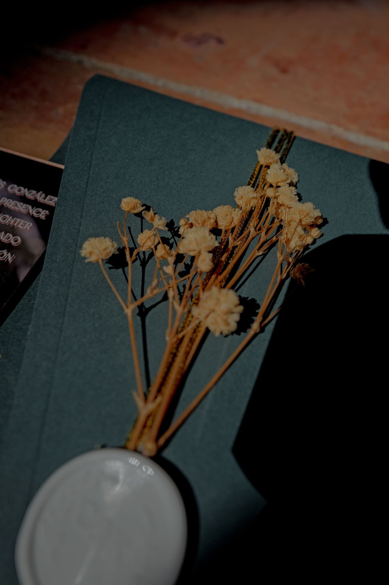 Dried baby's breath flowers in a small white vase on a teal notebook at a wedding reception.