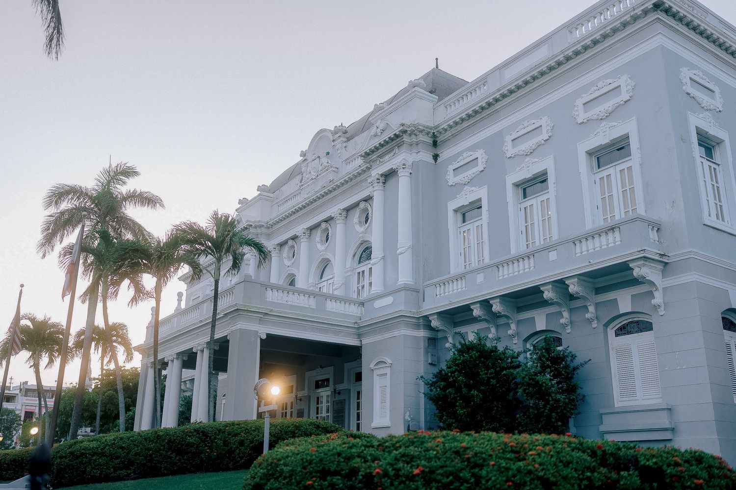 Grand white neoclassical building surrounded by palm trees at dusk, elegant wedding venue exterior.