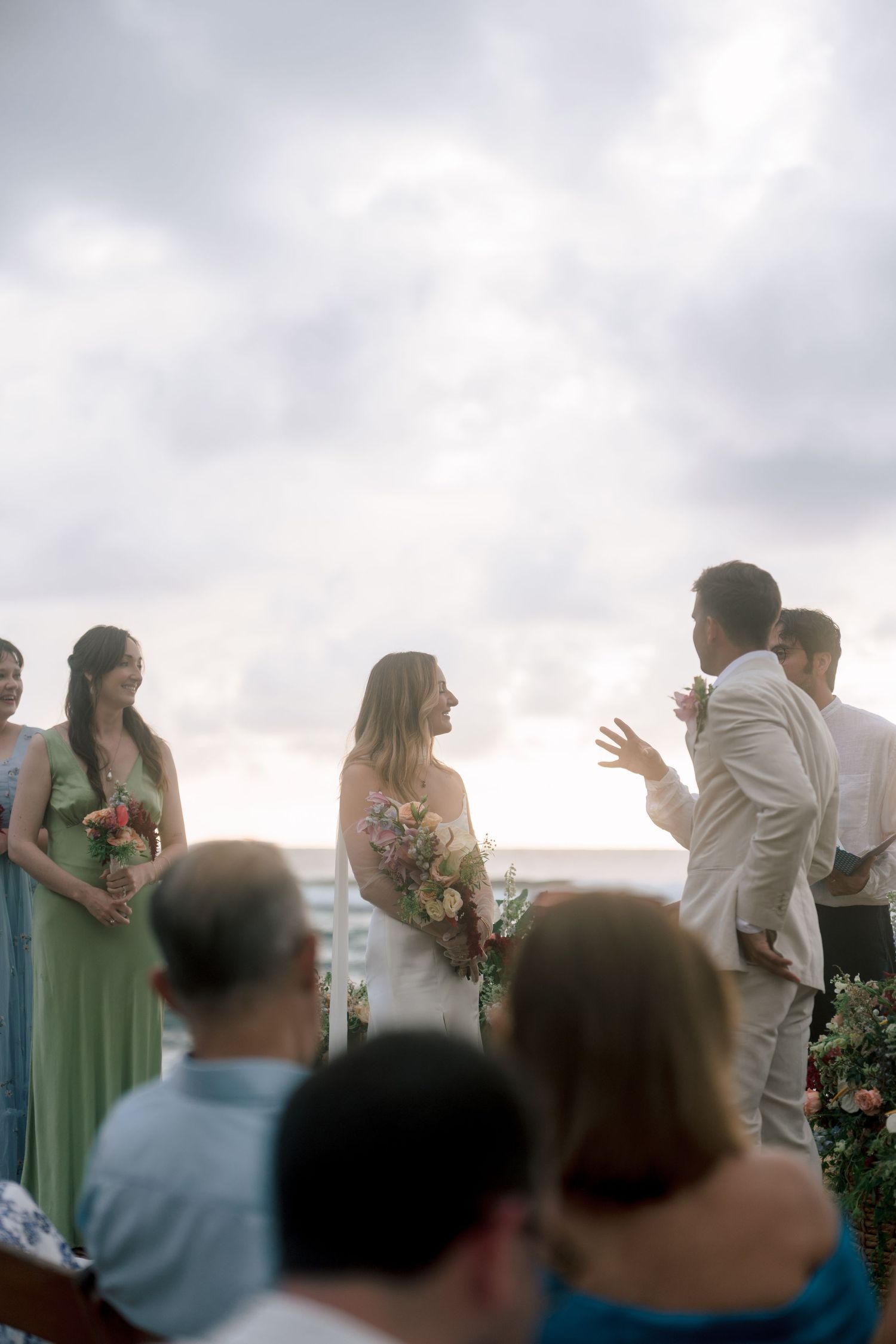 Bride and groom exchange vows at an outdoor beach wedding ceremony under a cloudy sky.