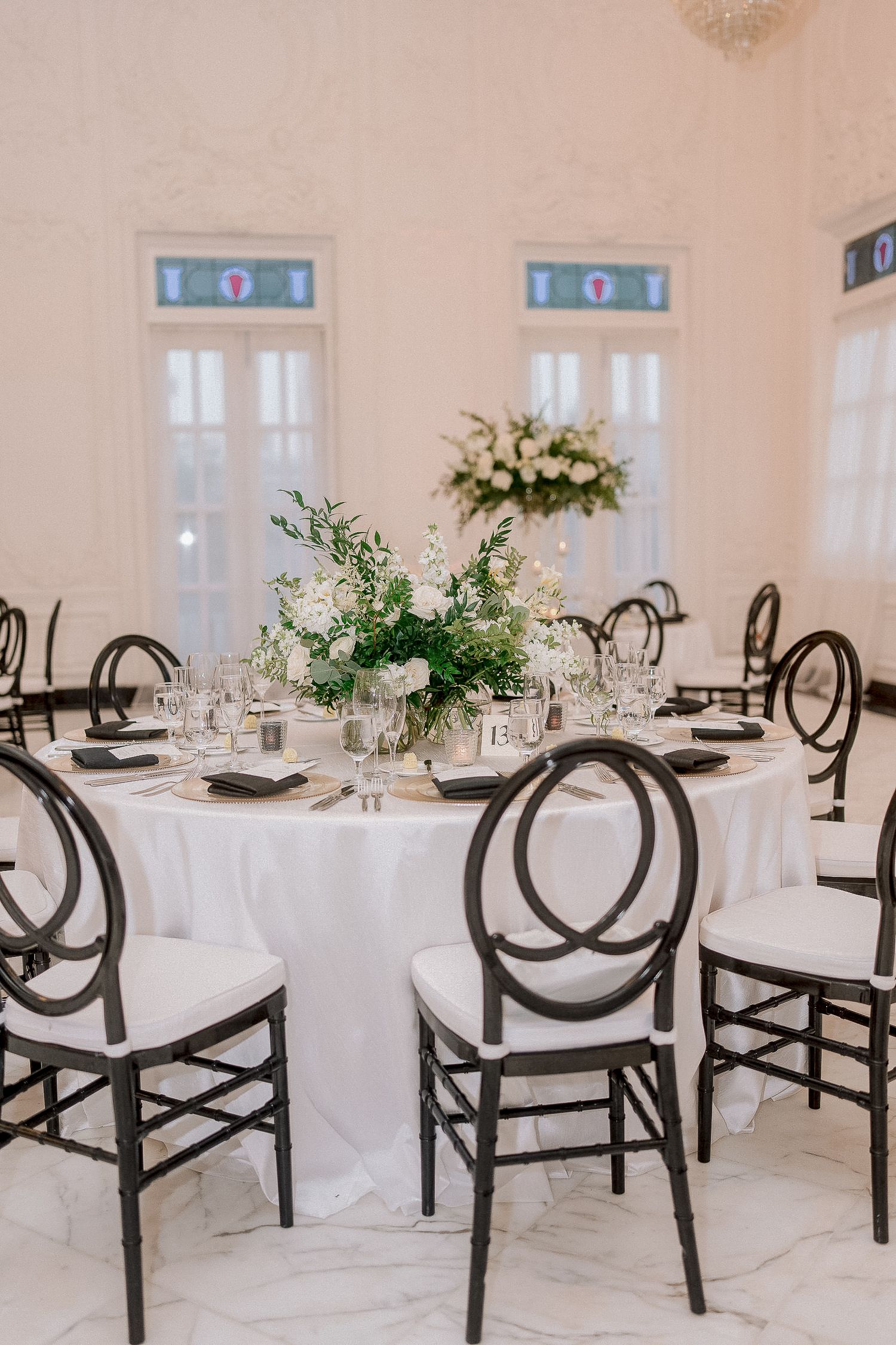 Elegant wedding reception round tables with black chairs and lush greenery floral centerpieces.