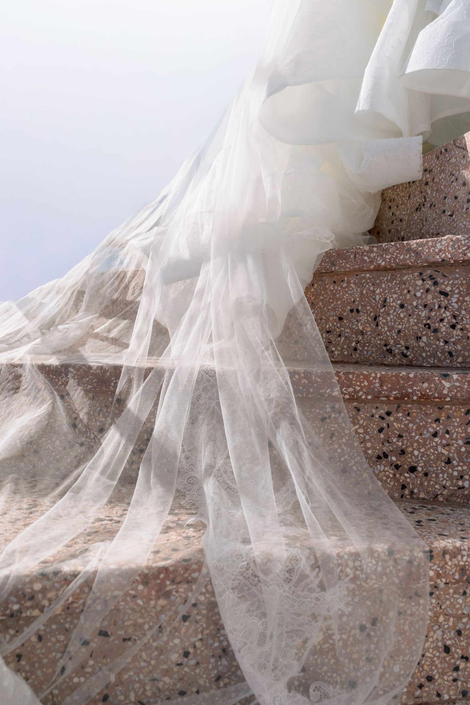 Flowing white wedding veil draped elegantly over stone steps, creating a dreamy bridal scene.