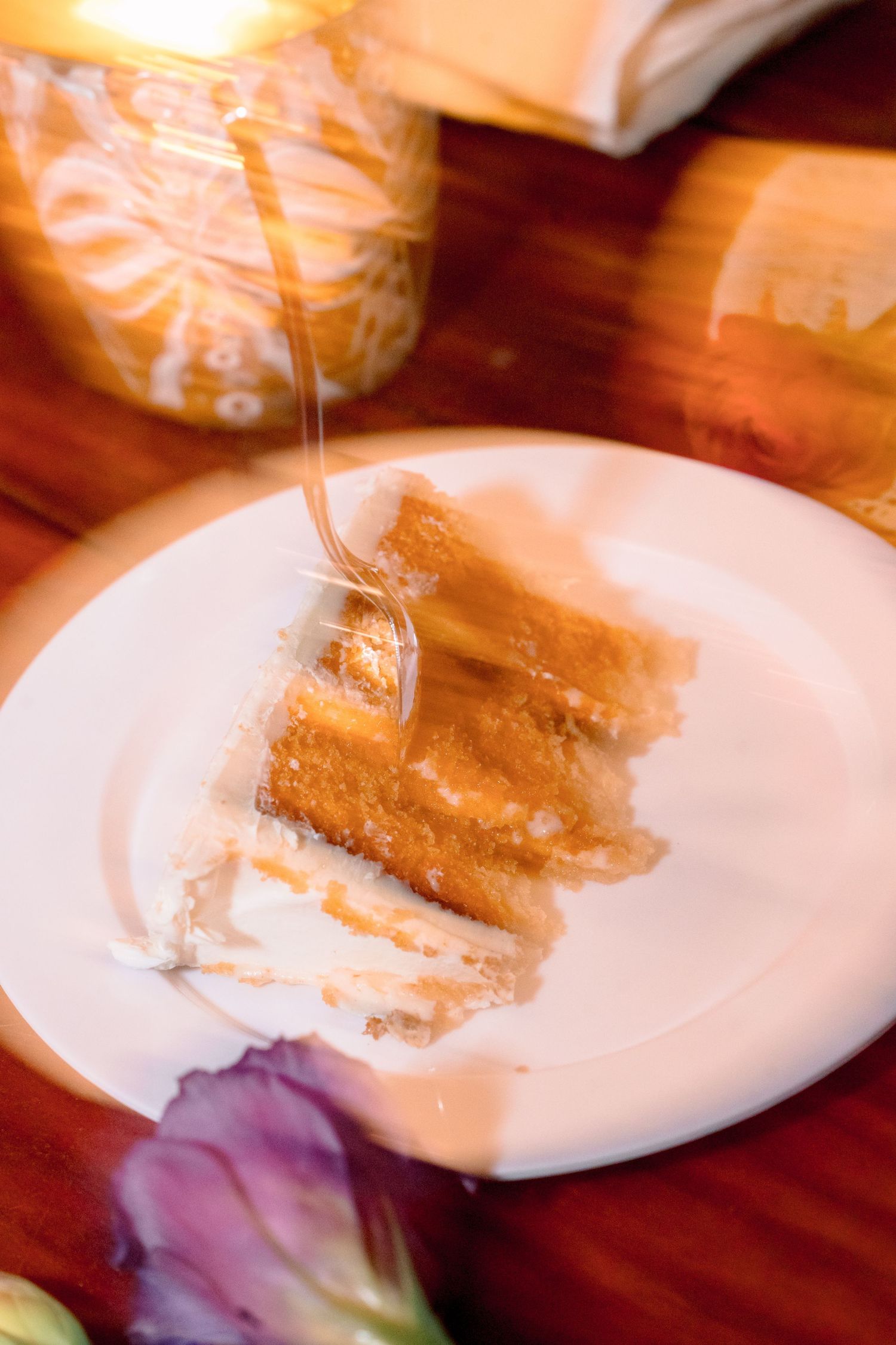 A slice of layered cake with honey drizzle on a white plate, with a candle in the background.