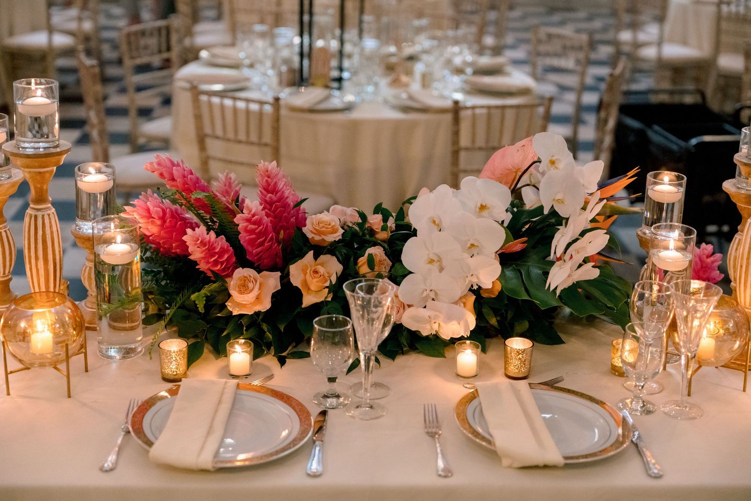 Elegant wedding reception table with tropical floral centerpiece featuring pink ginger, white orchids, and candles.