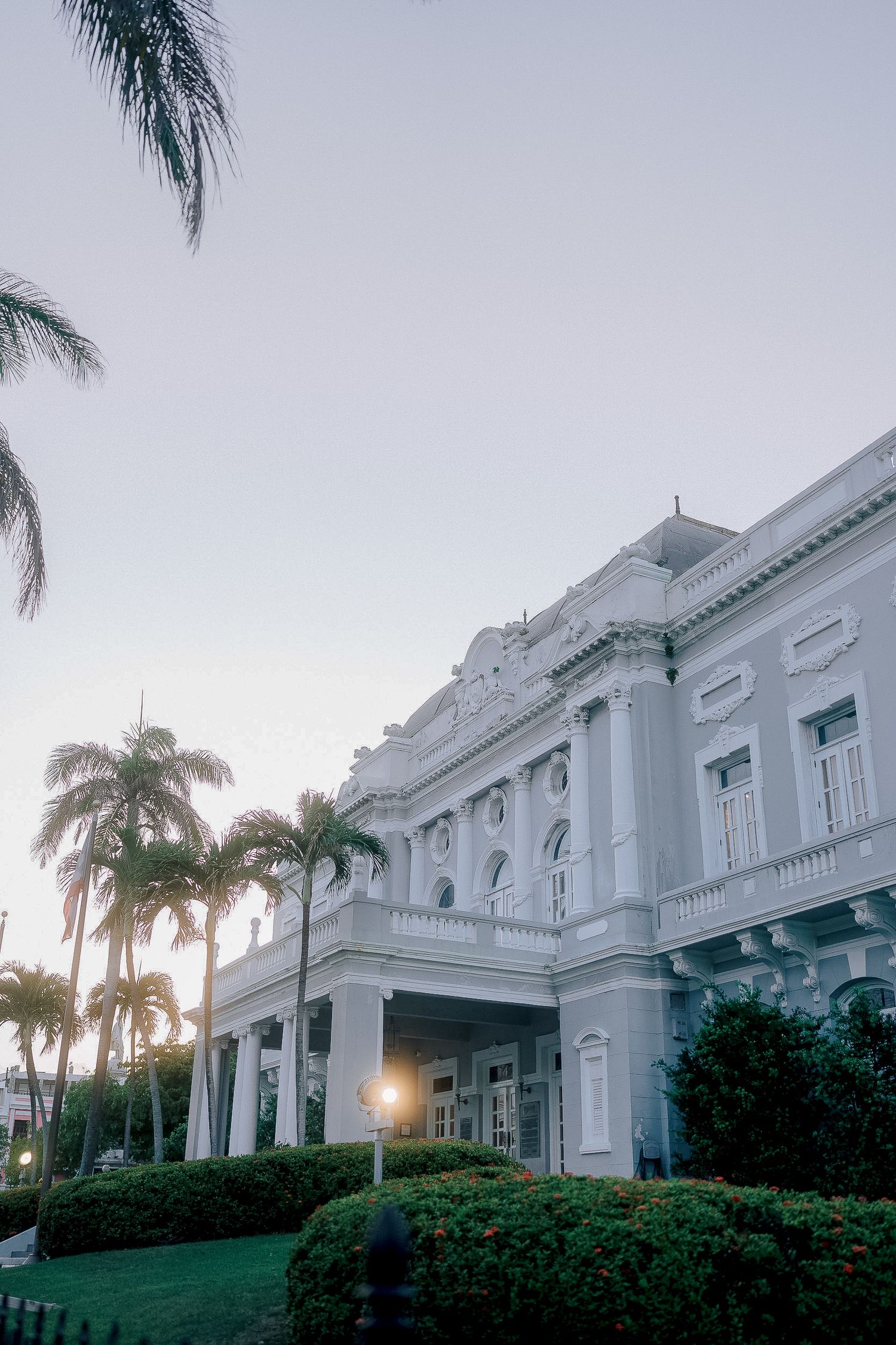 Grand white neoclassical building with palm trees and manicured gardens at sunset wedding venue.