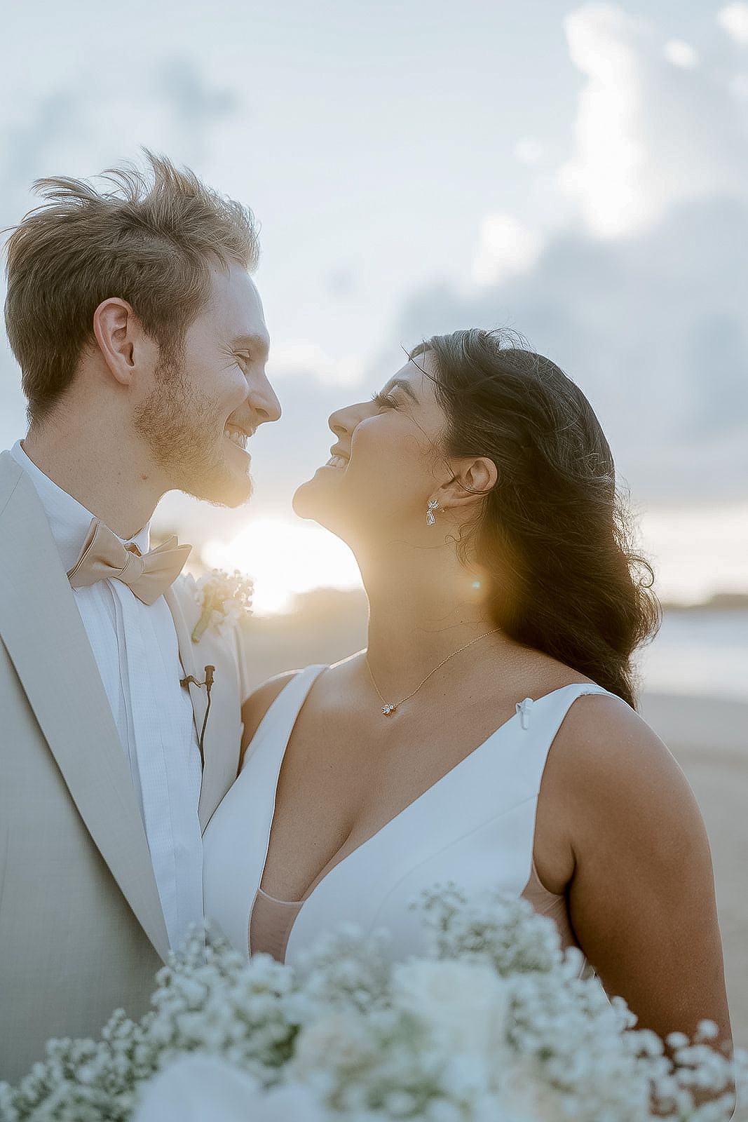 A smiling bride and groom share a romantic moment on a beach at golden sunset hour.