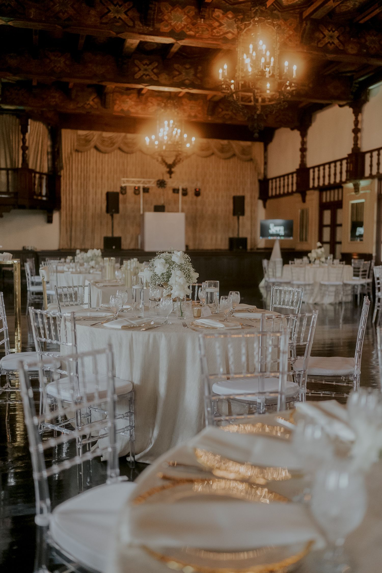 Elegant wedding reception hall with chandelier, white chiavari chairs, and floral centerpieces.