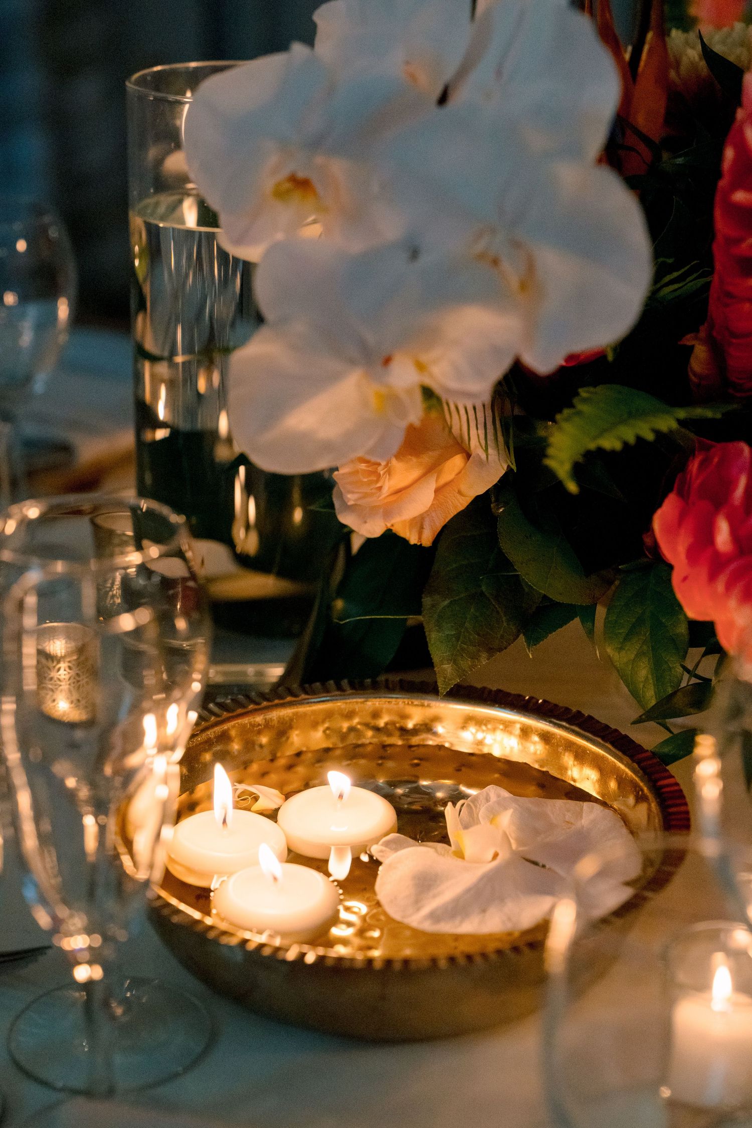 Elegant wedding table with floating candles in gold tray, white orchids, and glowing candlelight centerpiece.