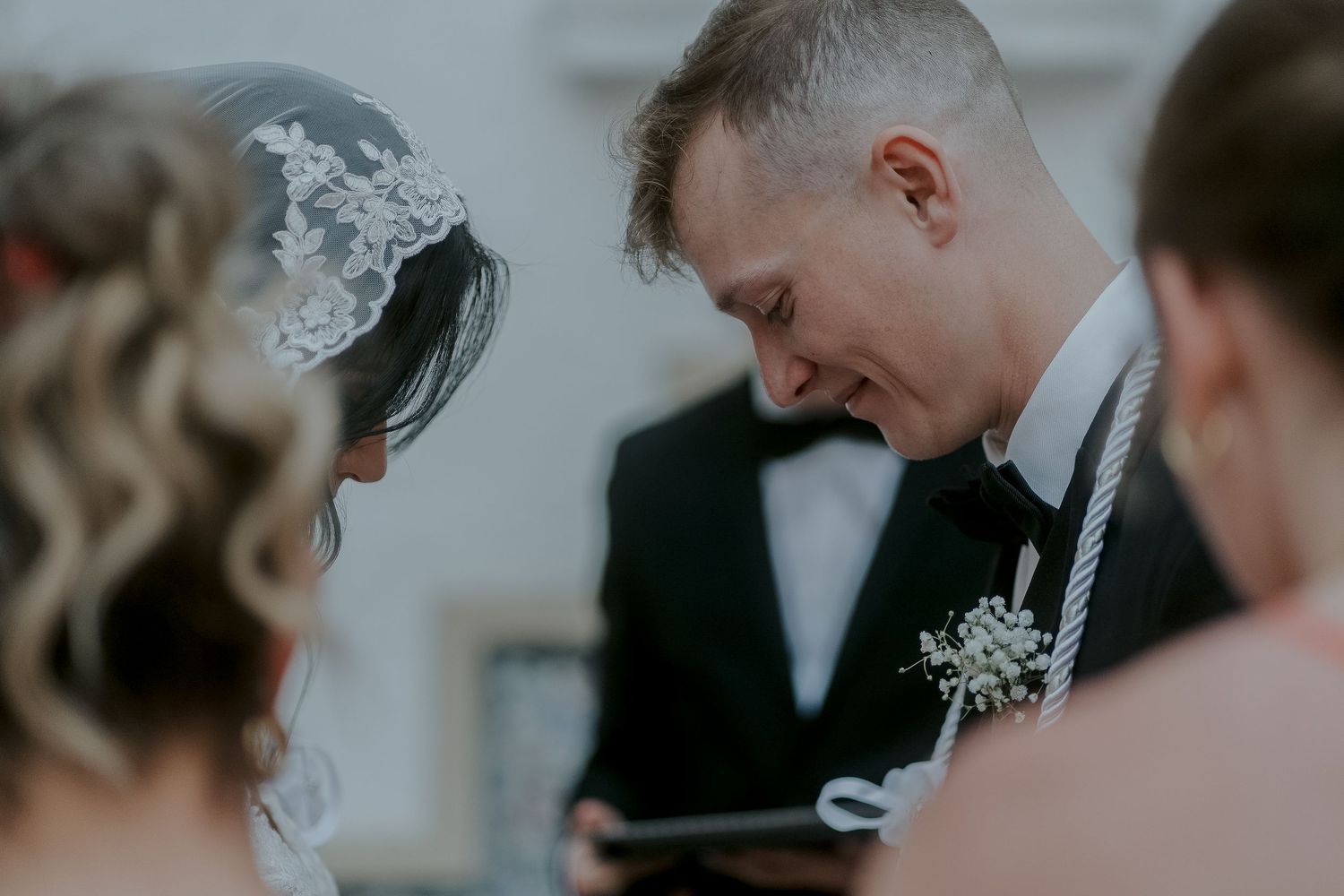 Bride and groom share an emotional moment during wedding ceremony, groom in black tuxedo with boutonniere.
